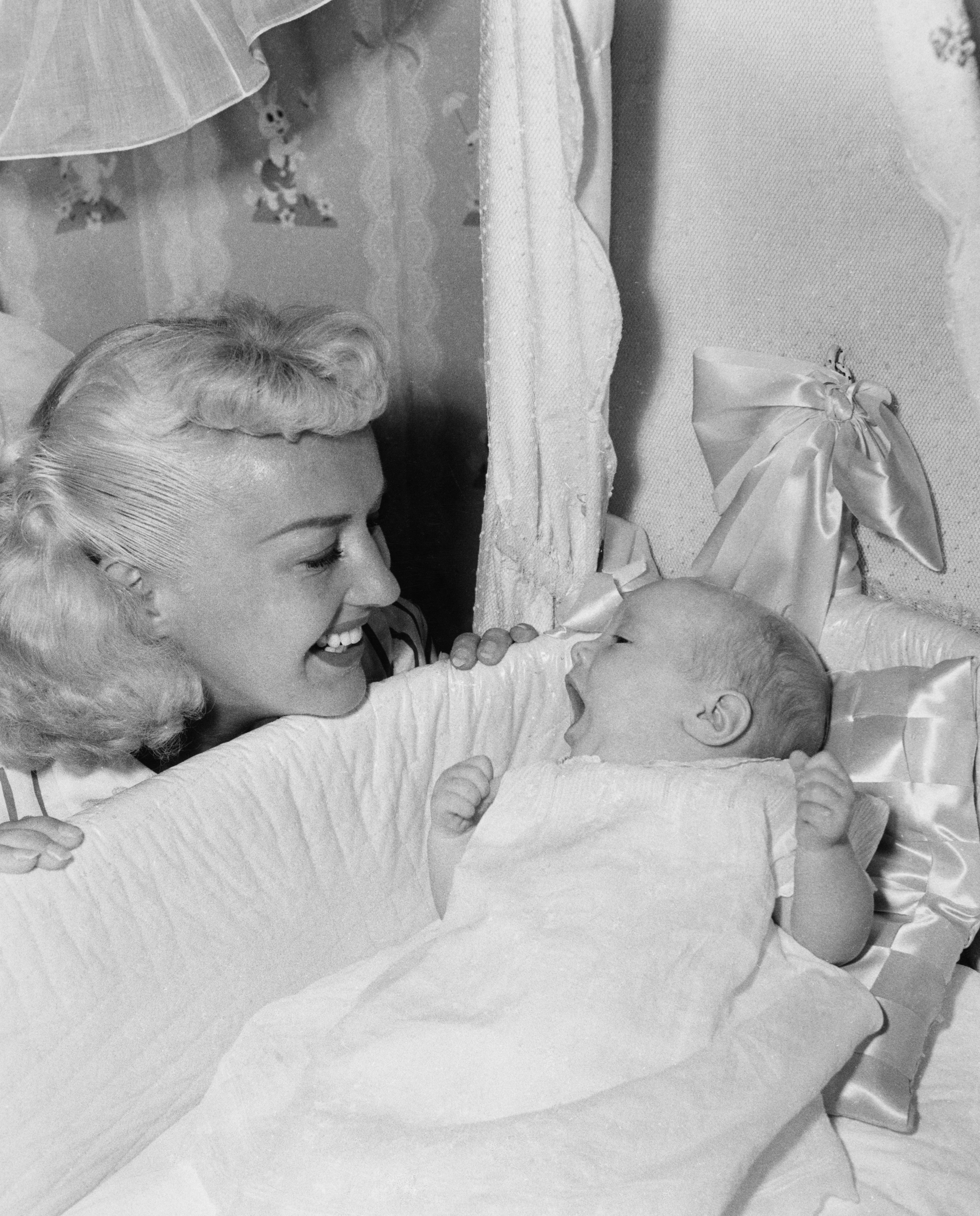 Betty Grable smiles down at her baby daughter in her crib
