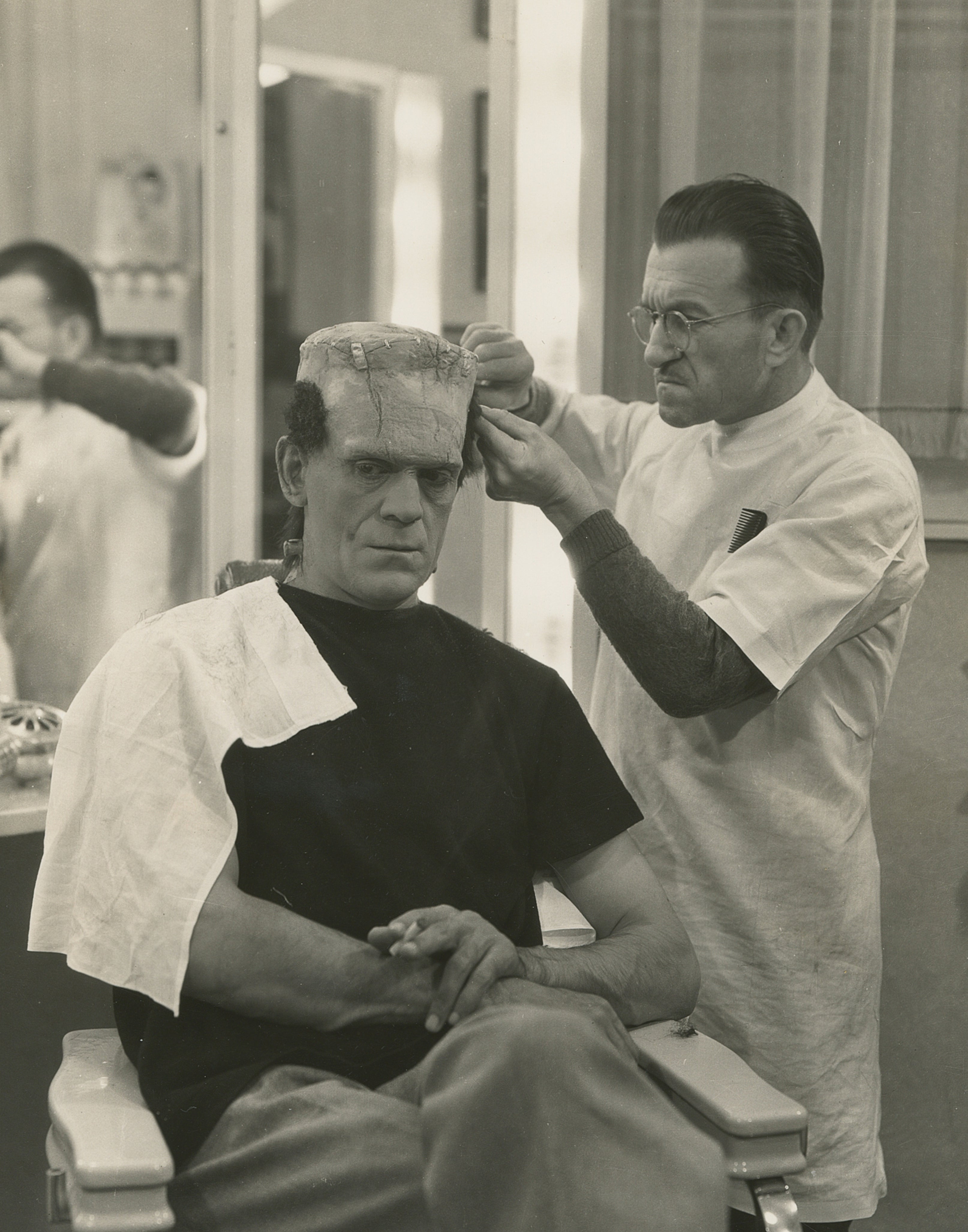 Boris Karloff having makeup applied as Frankenstein's monster in a makeup chair
