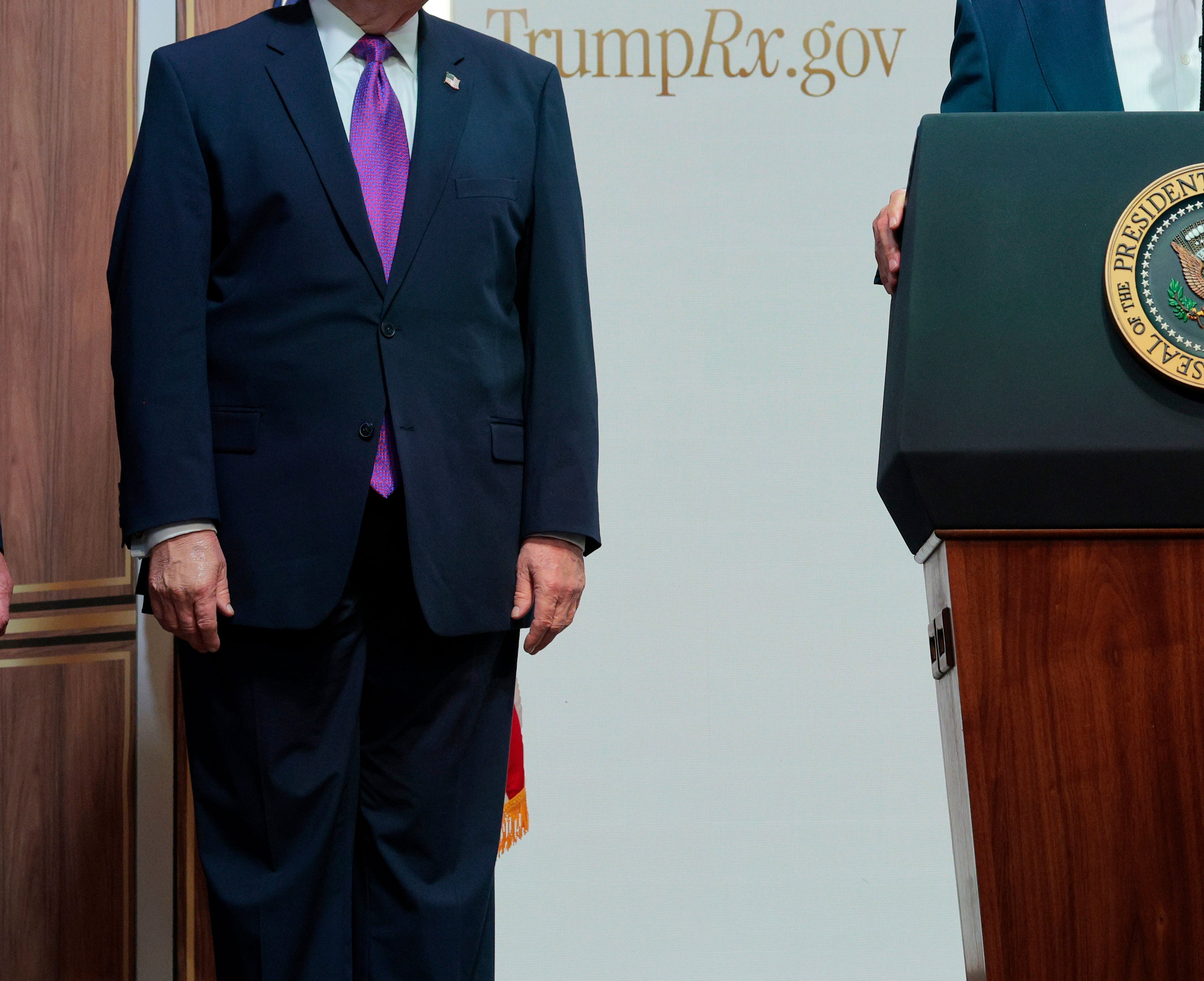 RFK Jr. and Donald Trump standing next to each other in suits at the TrumpRx press conference, in front of a wood-paneled background and Trump Rx logo to one side