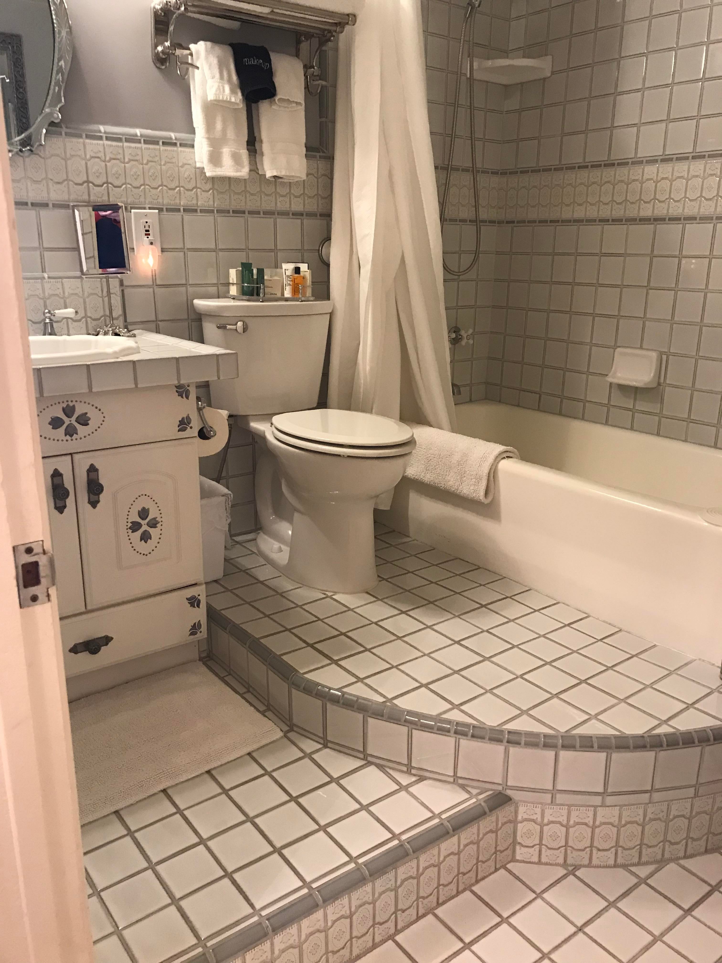 Bathroom with tiled floor, bathtub, shower, toilet, and vanity sink. Towels and toiletries are neatly arranged