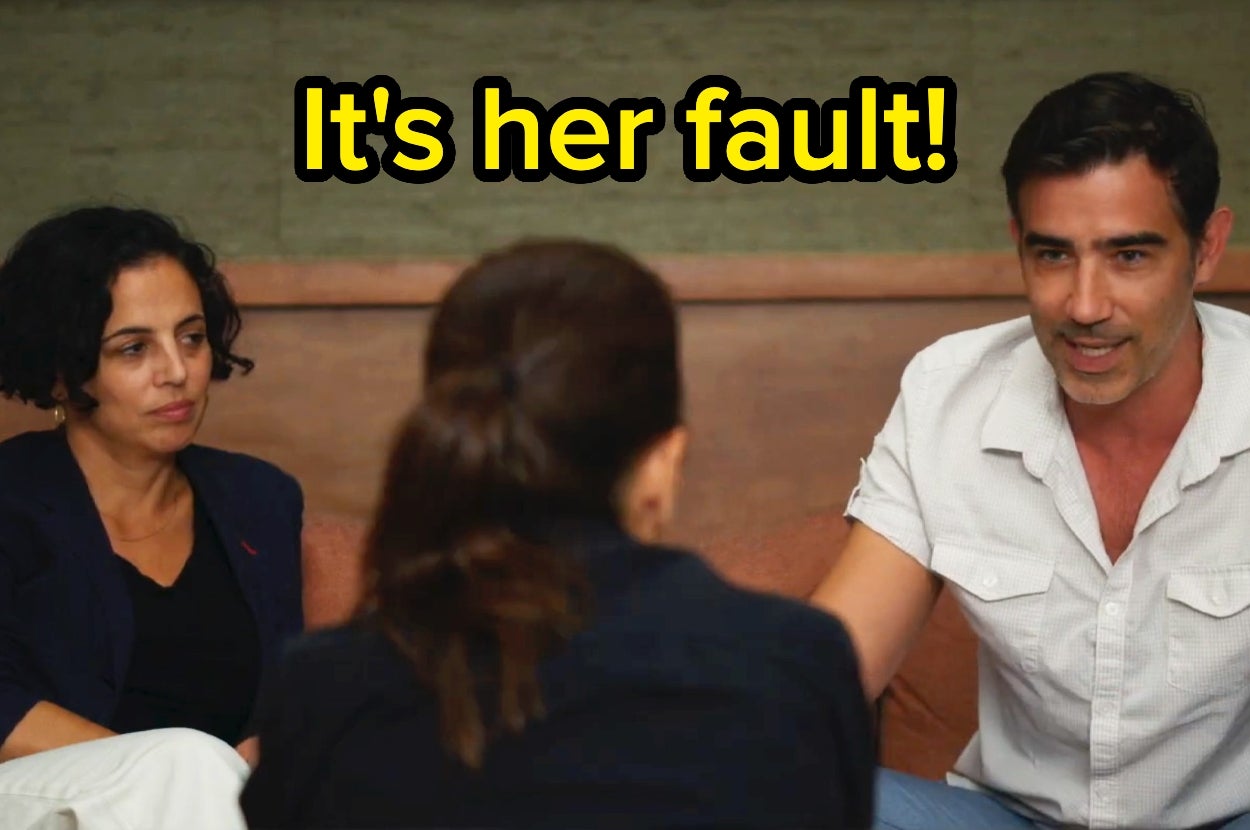 Two people listen to a man saying, "It's her fault!" in a tense discussion setting
