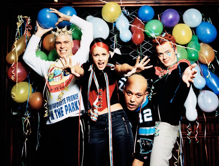 Four people in quirky, playful poses with balloons and streamers in the background, creating a festive atmosphere