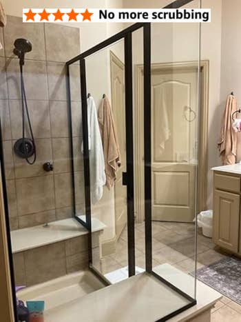 Glass shower enclosure with black frame, tiled walls, and a towel hanging outside.