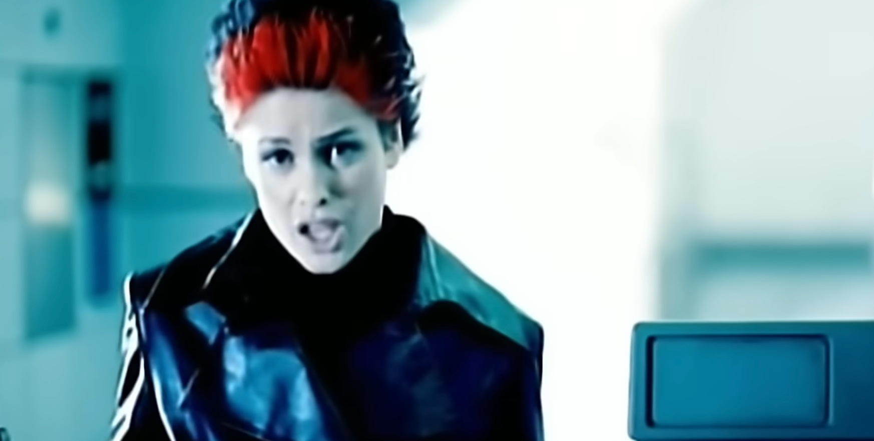 Person with spiky hair and a leather jacket sings passionately in a dimly lit setting