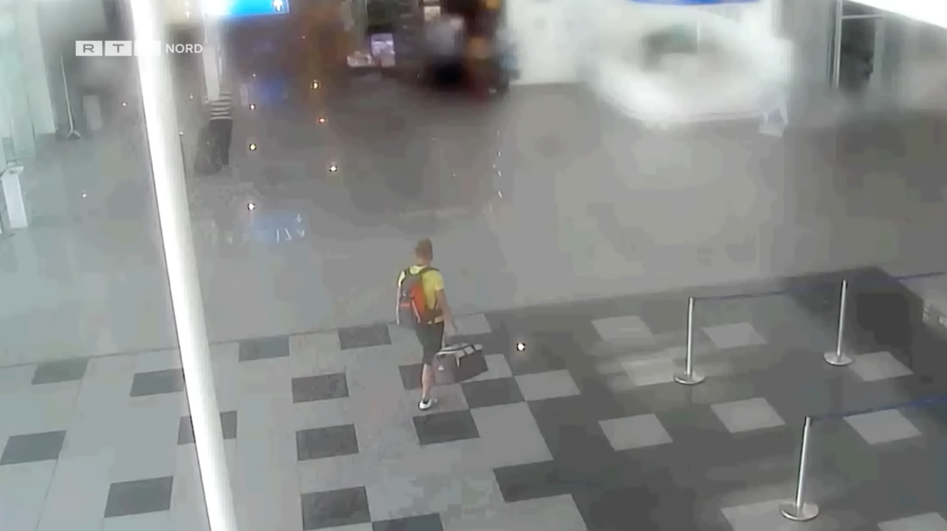 A person with a backpack walks through an airport terminal, seen from above. The area is quiet with no other visible people nearby