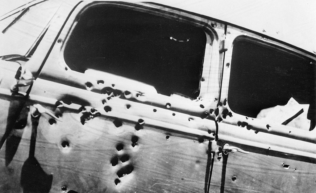 Old car with numerous bullet holes on the side and windows, suggesting a violent encounter
