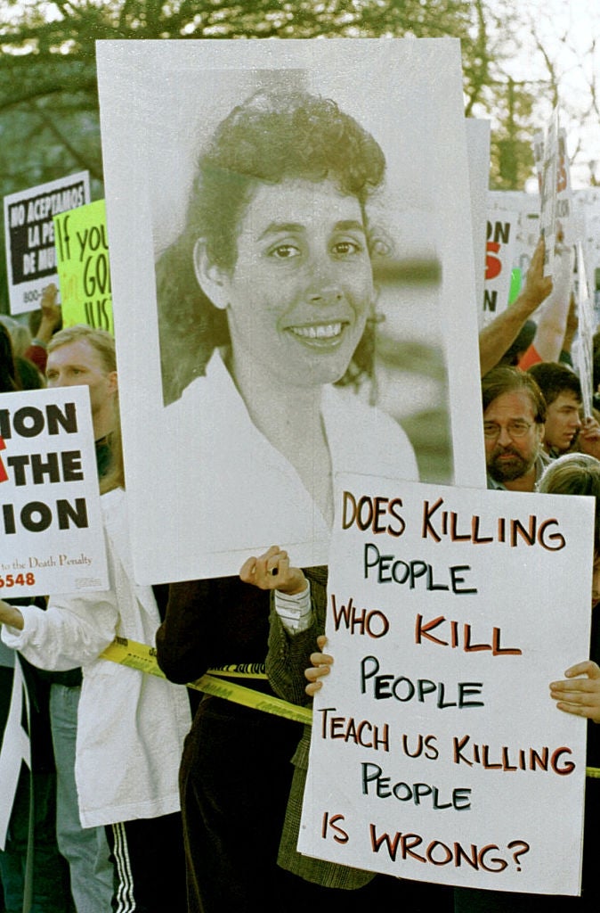 Protesters hold signs, including one with a large portrait of a woman and another questioning the effectiveness of the death penalty