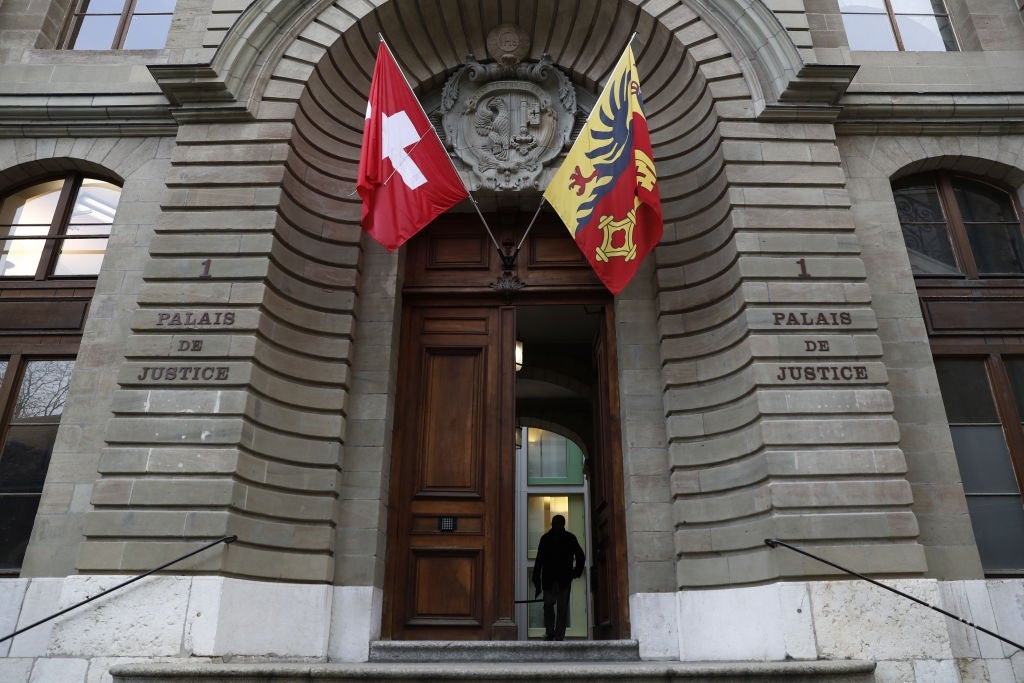 Entrance to a courthouse with Swiss and Geneva flags. A person is walking through the doorway