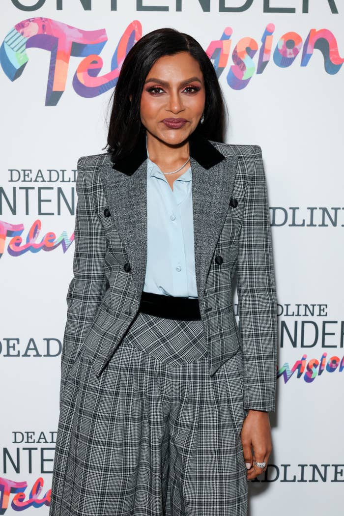 Person in a plaid suit with wide-legged pants at a celebrity event, standing against a backdrop with "Deadline Contenders Television" text