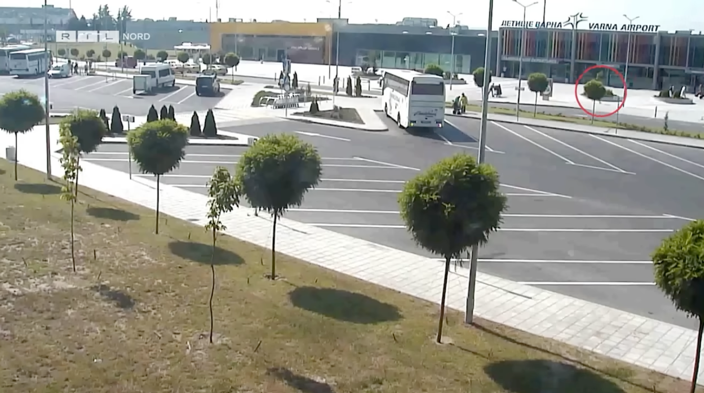 Bus terminal in front of an airport with buses parked and some people walking outside the terminal building