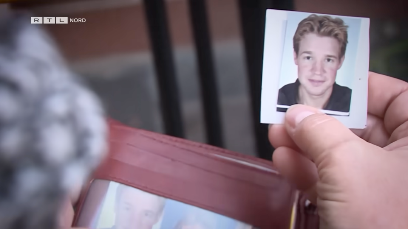 Person holding a small photo from a wallet, featuring a young man's headshot
