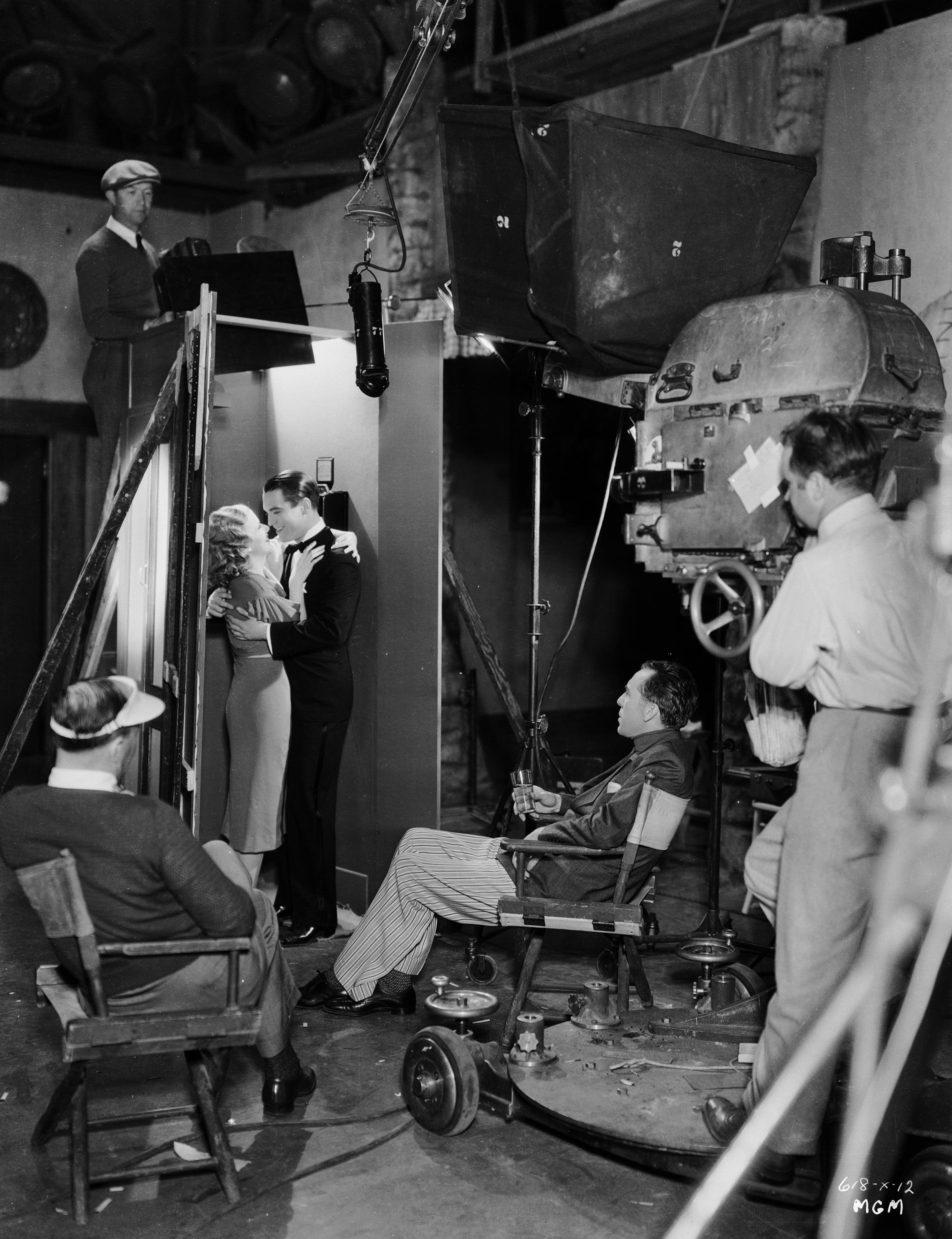 Jean Harlow and Chester Morris in formal attire perform a dramatic scene on set while Jack Conway watches them in his director chair
