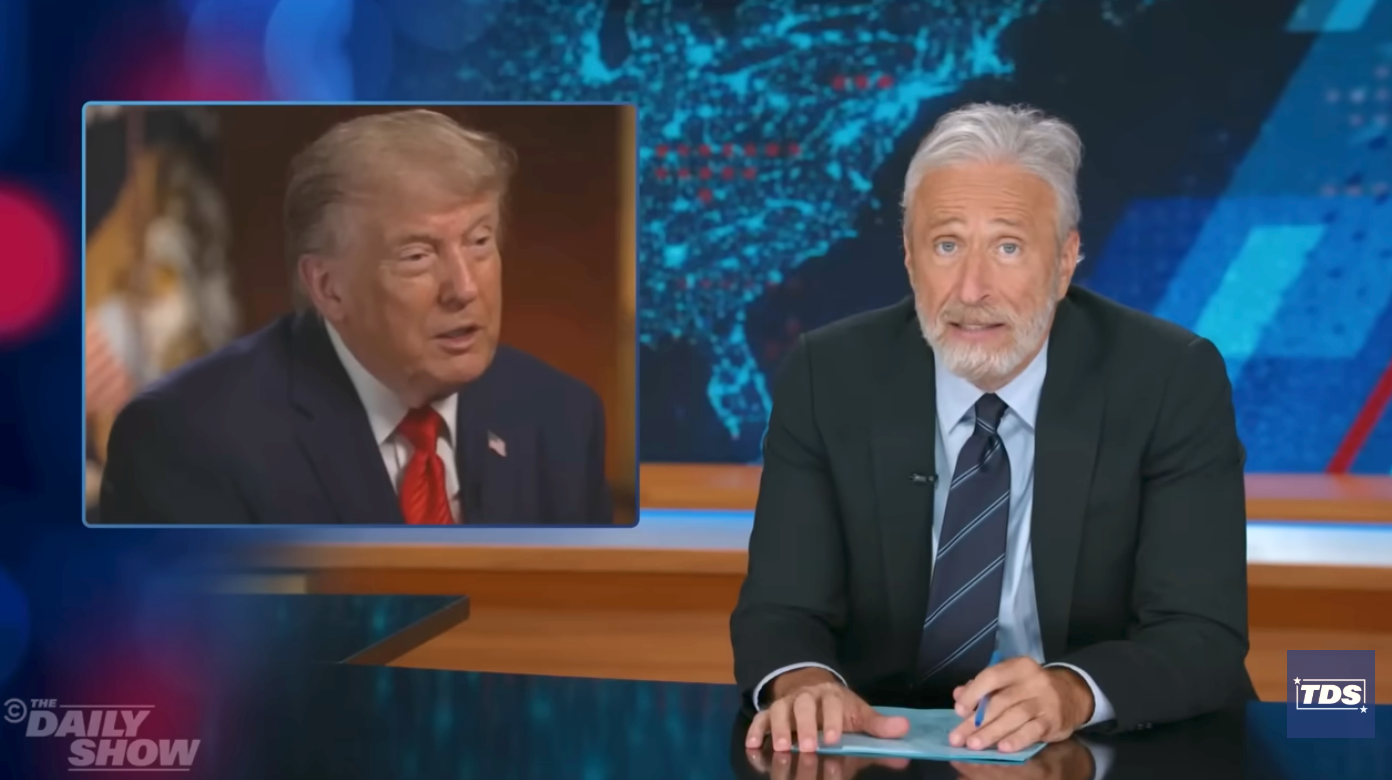 A TV host sitting at a desk comments on an interview clip of a former U.S. president shown on a screen beside him