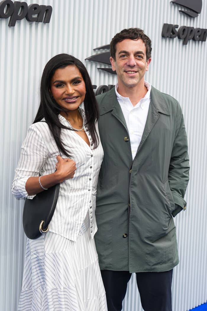 Two people pose together at an event. One is wearing a striped dress and pearls, and the other a casual jacket and shirt