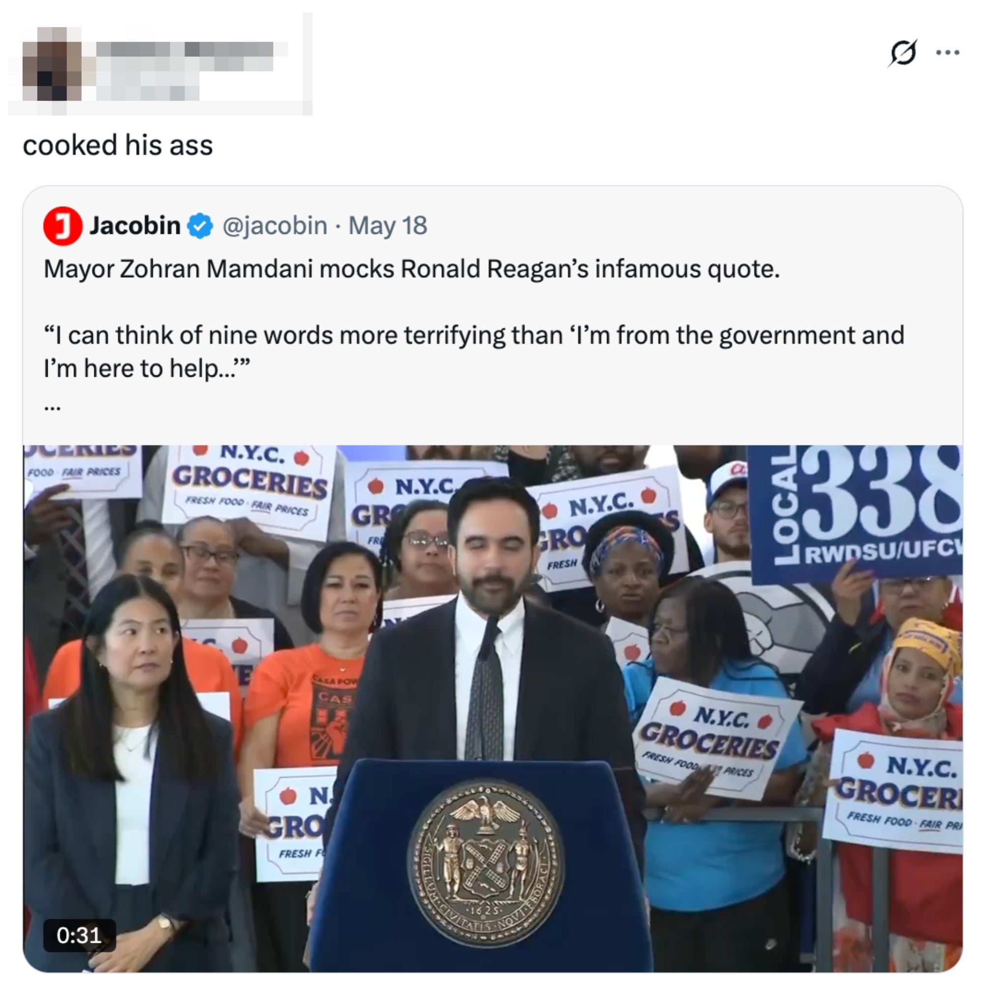 Mayor Zohra Mamdani speaks at a podium, surrounded by supporters holding N.Y.C. grocery signs