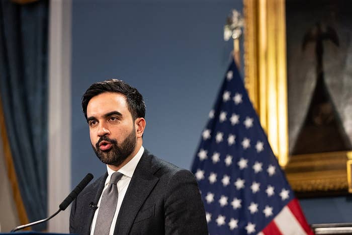A man in a suit speaks at a podium with a U.S. flag in the background