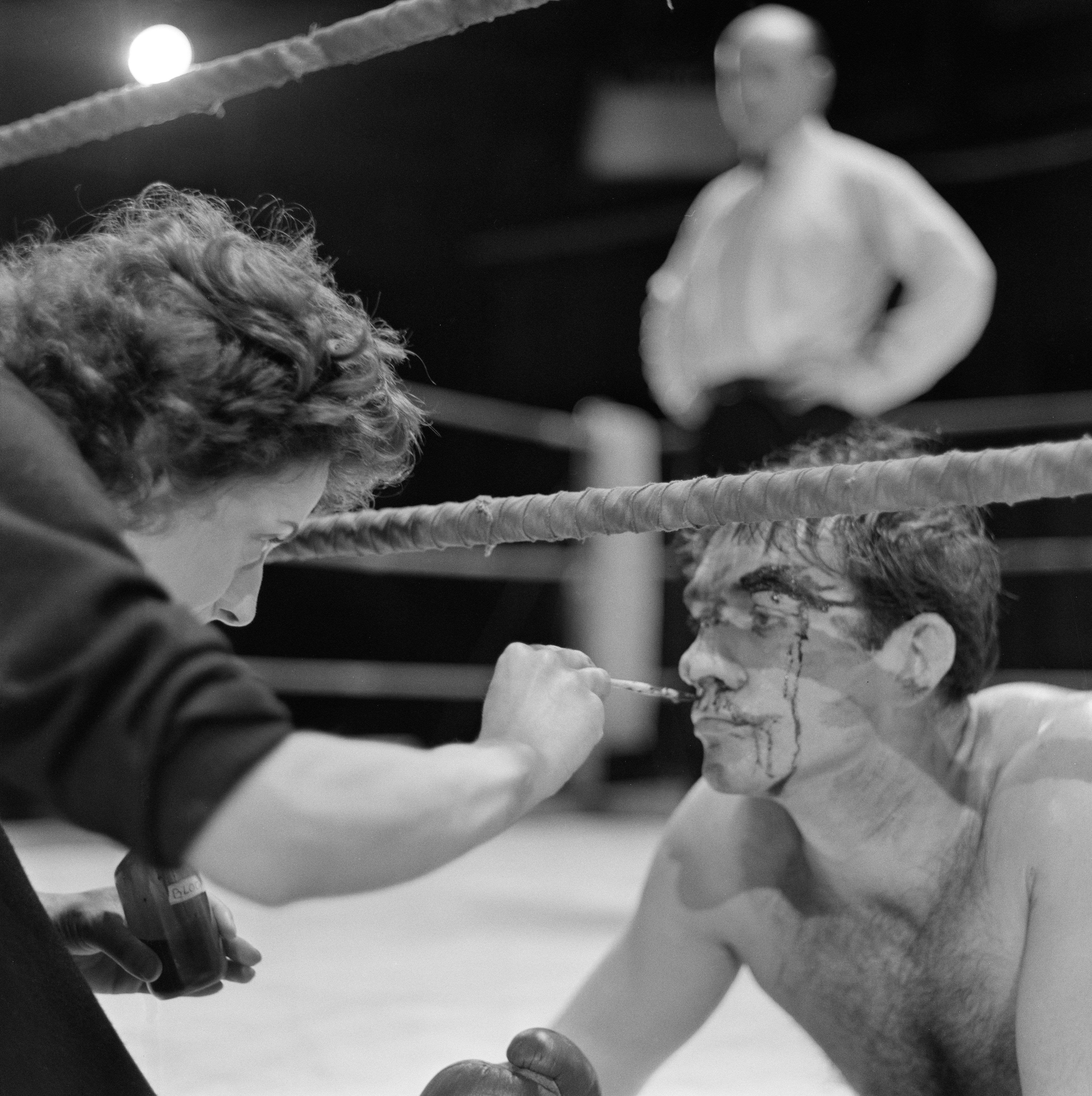 Makeup artist Jill Summers applying fake blood to Sean Connery as he lays on his stomach in a boxing ring