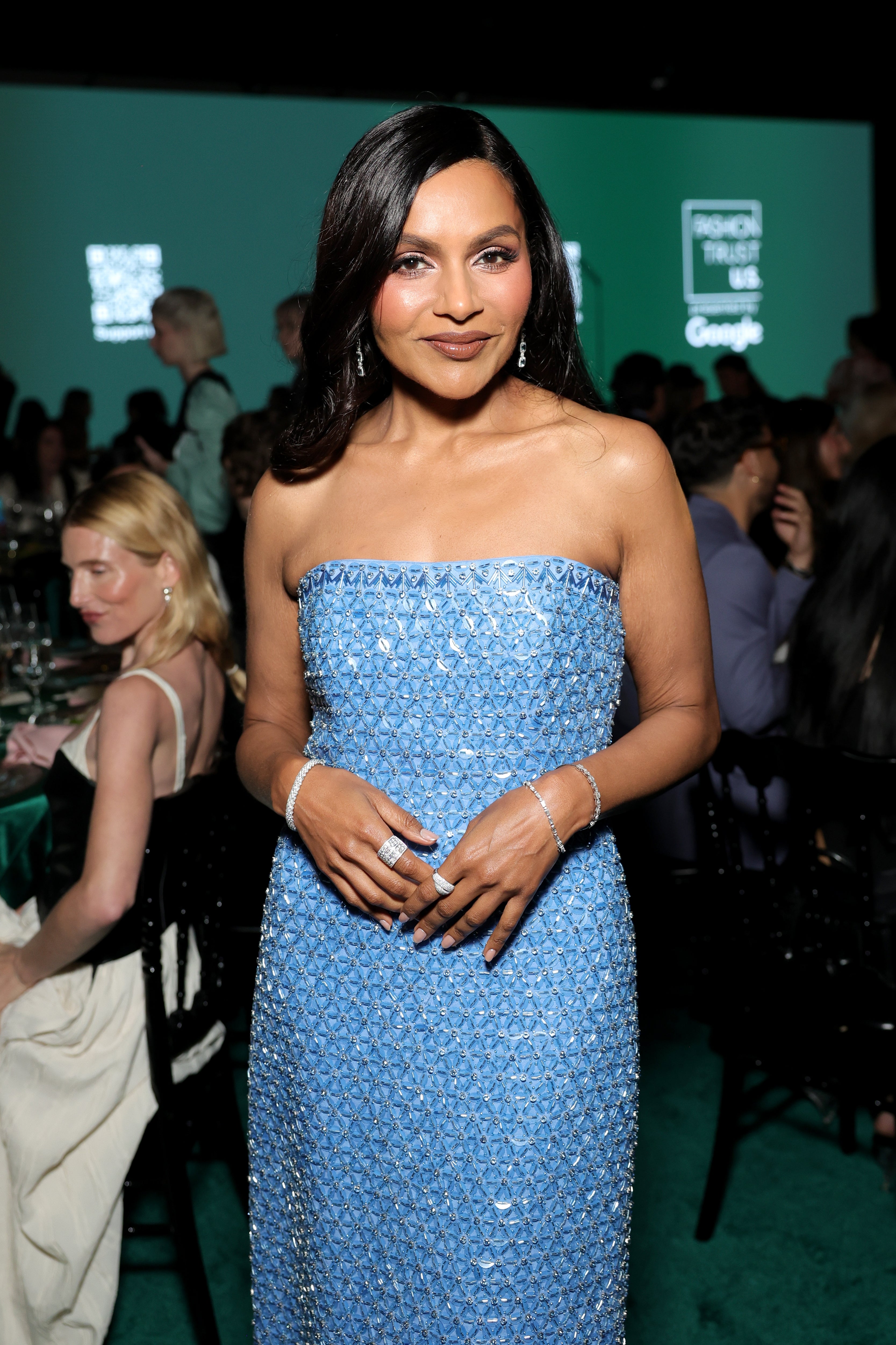 A person in an elegant, strapless dress poses at an event, wearing minimal jewelry and exuding confidence and style