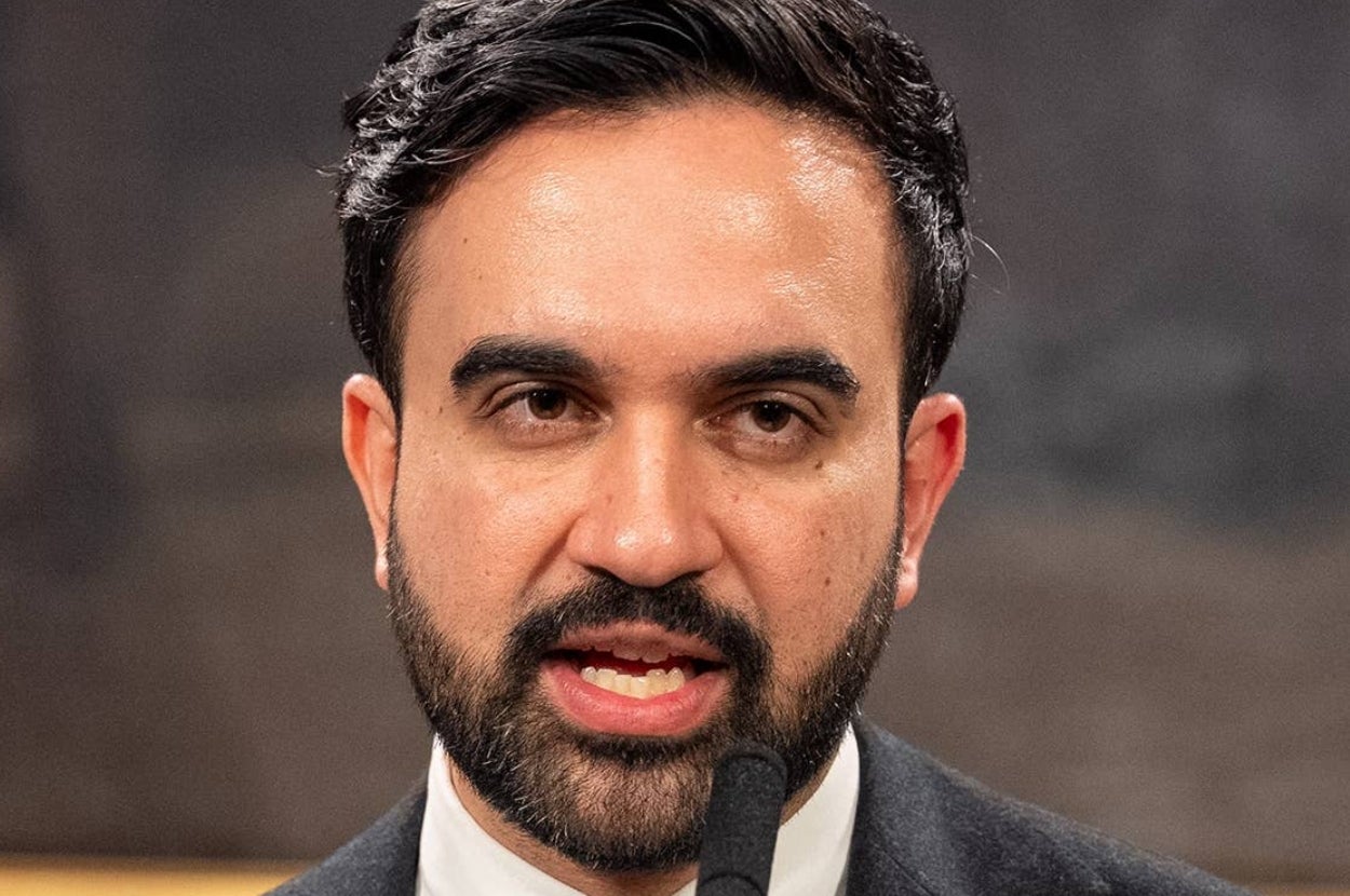 A person speaking into a microphone, dressed in a formal suit, with a focused expression