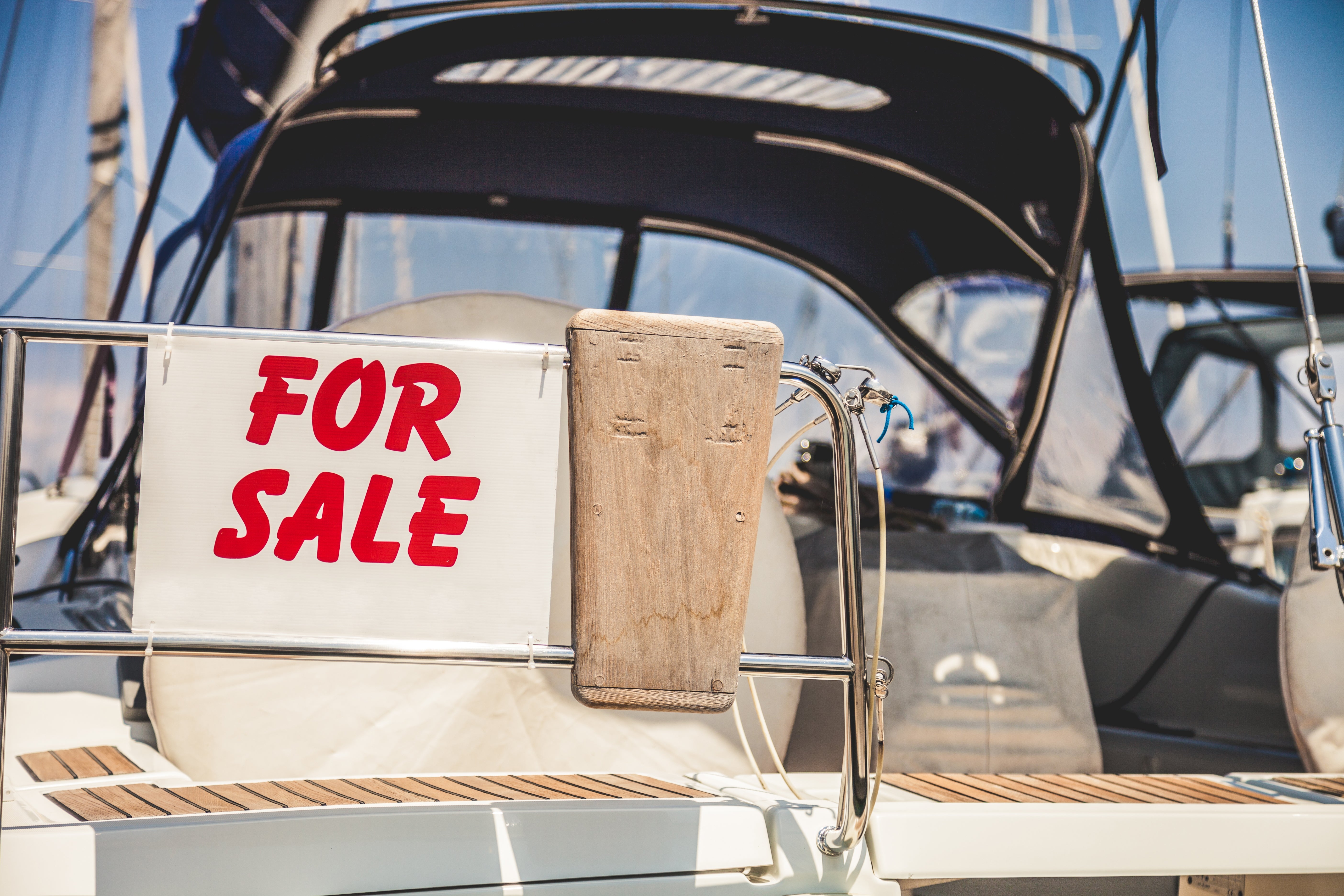 Boat with a "For Sale" sign on the stern, docked at a marina