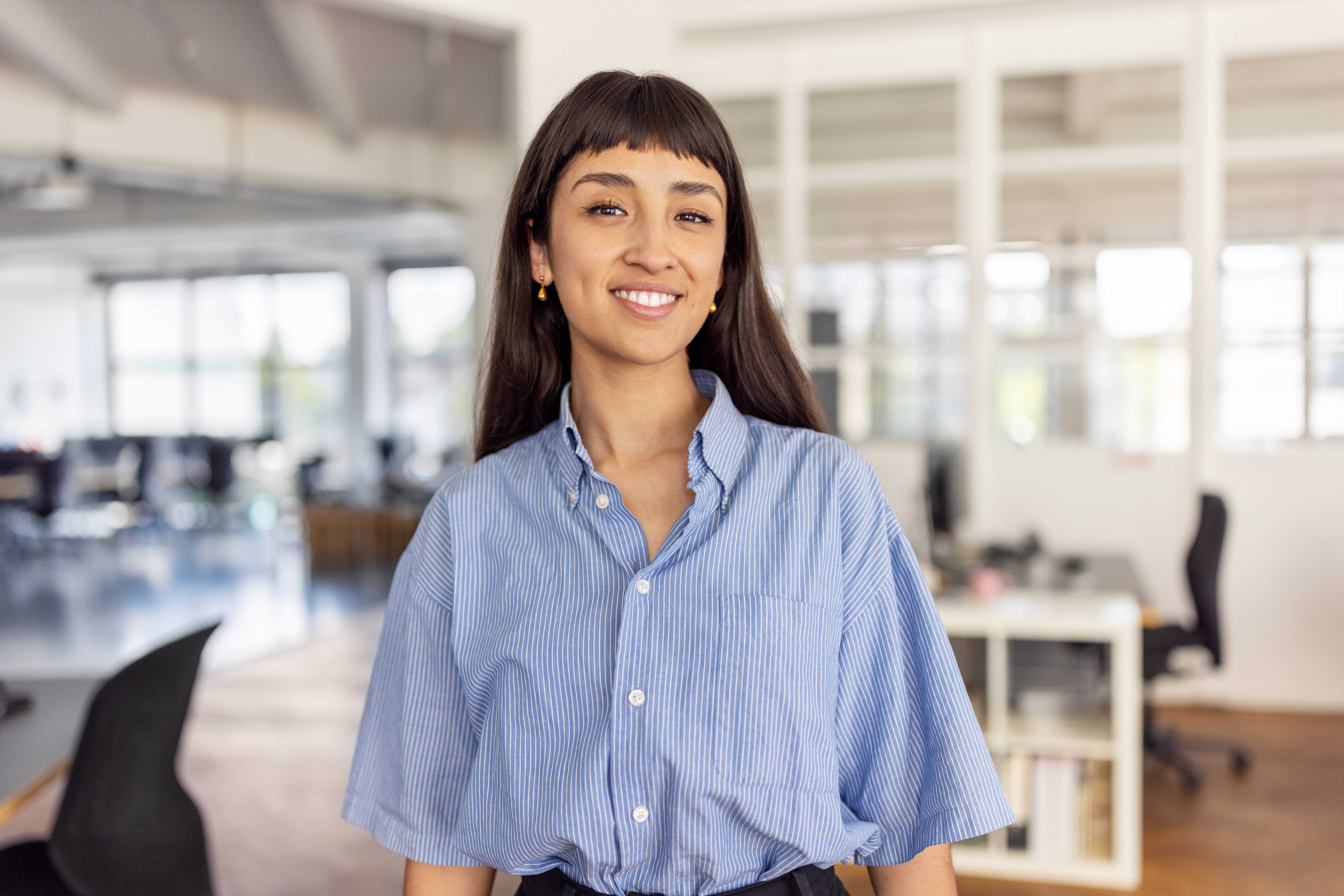 Person smiling in a modern office, wearing a striped, short-sleeve button-up shirt