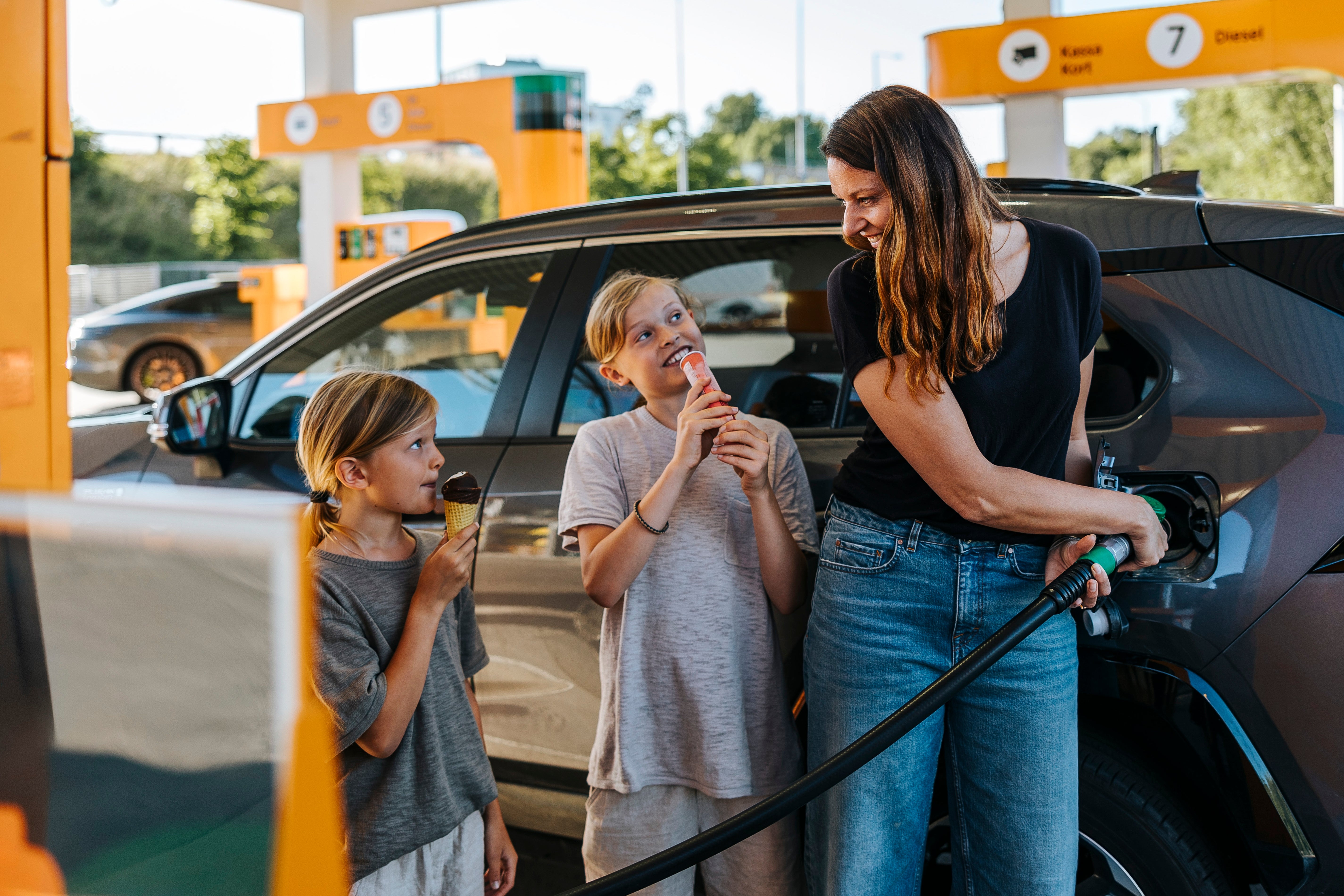 Woman refueling car while two kids enjoy ice cream at a gas station