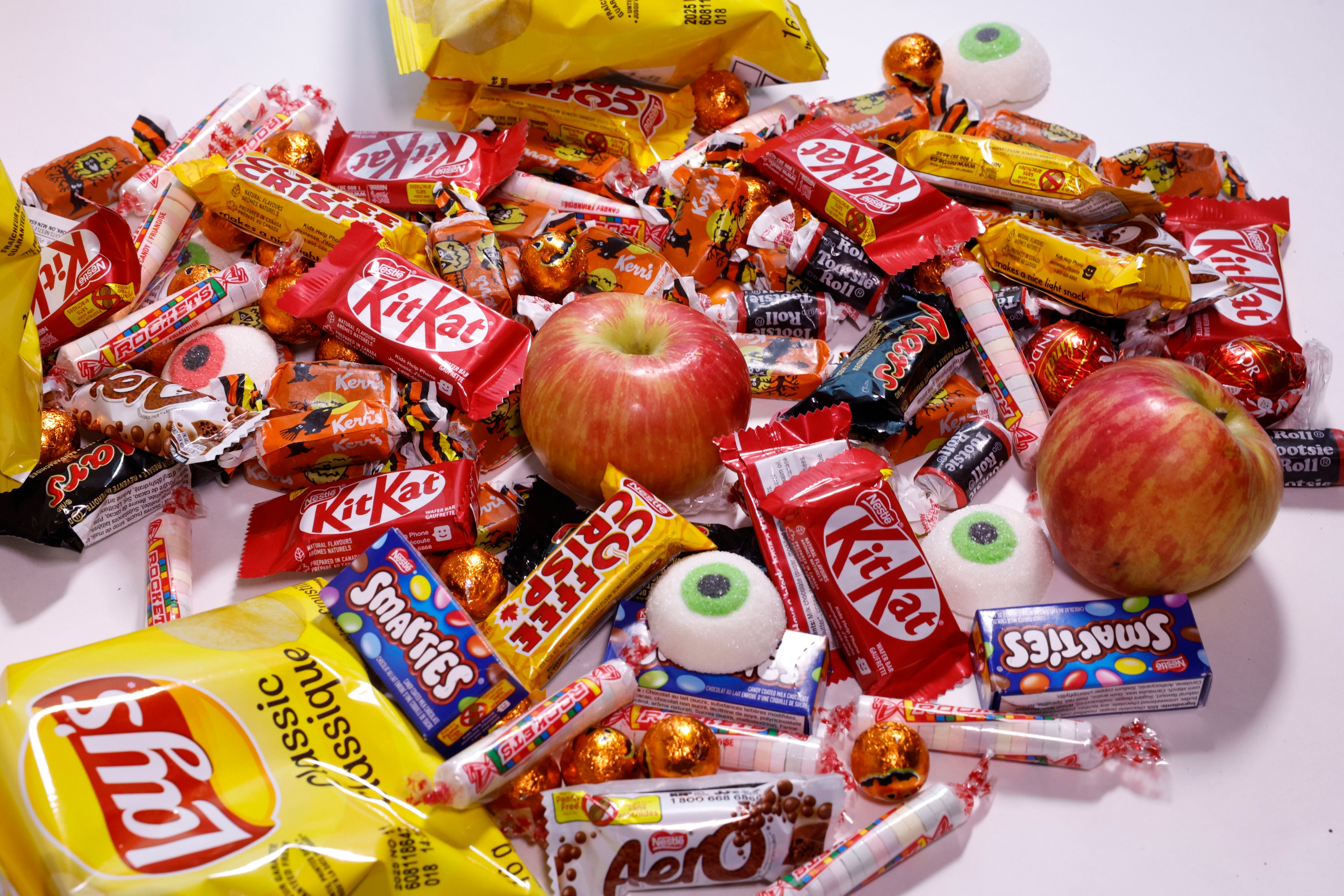 A variety of Halloween candies, including KitKats, Smarties, Aero bars, and Lay's chips, mixed with two apples and novelty eyeball candies