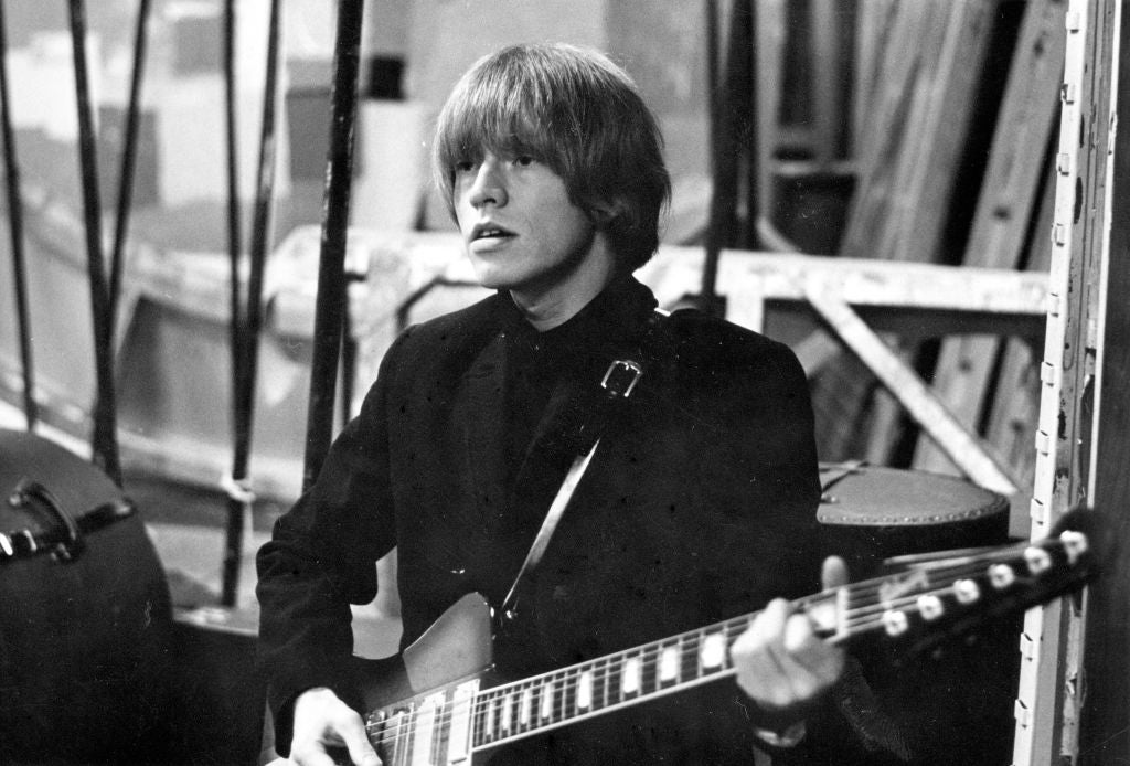 A idiosyncratic   with shaggy hairsbreadth  plays an electrical  guitar, wearing a sleek suit   jacket, with a focused look  successful  a backstage setting