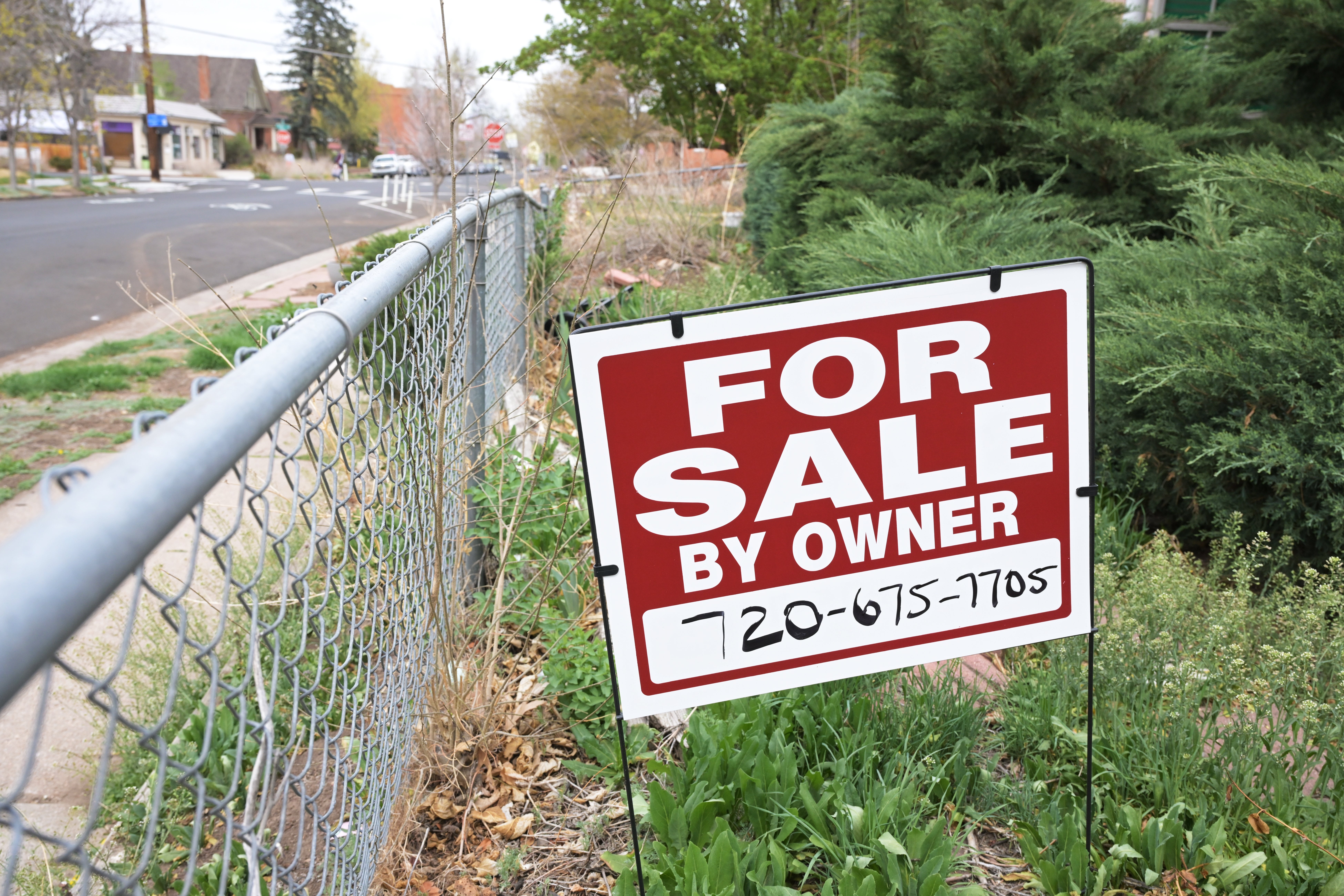 "For Sale By Owner" sign displayed in a yard near a street with a contact number listed