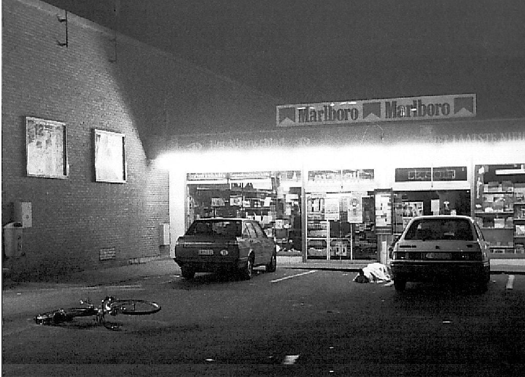 A nighttime country   extracurricular  a store, with 2  parked cars, a bicycle connected  the ground, and an unattended entity  resembling a broad  oregon  bag