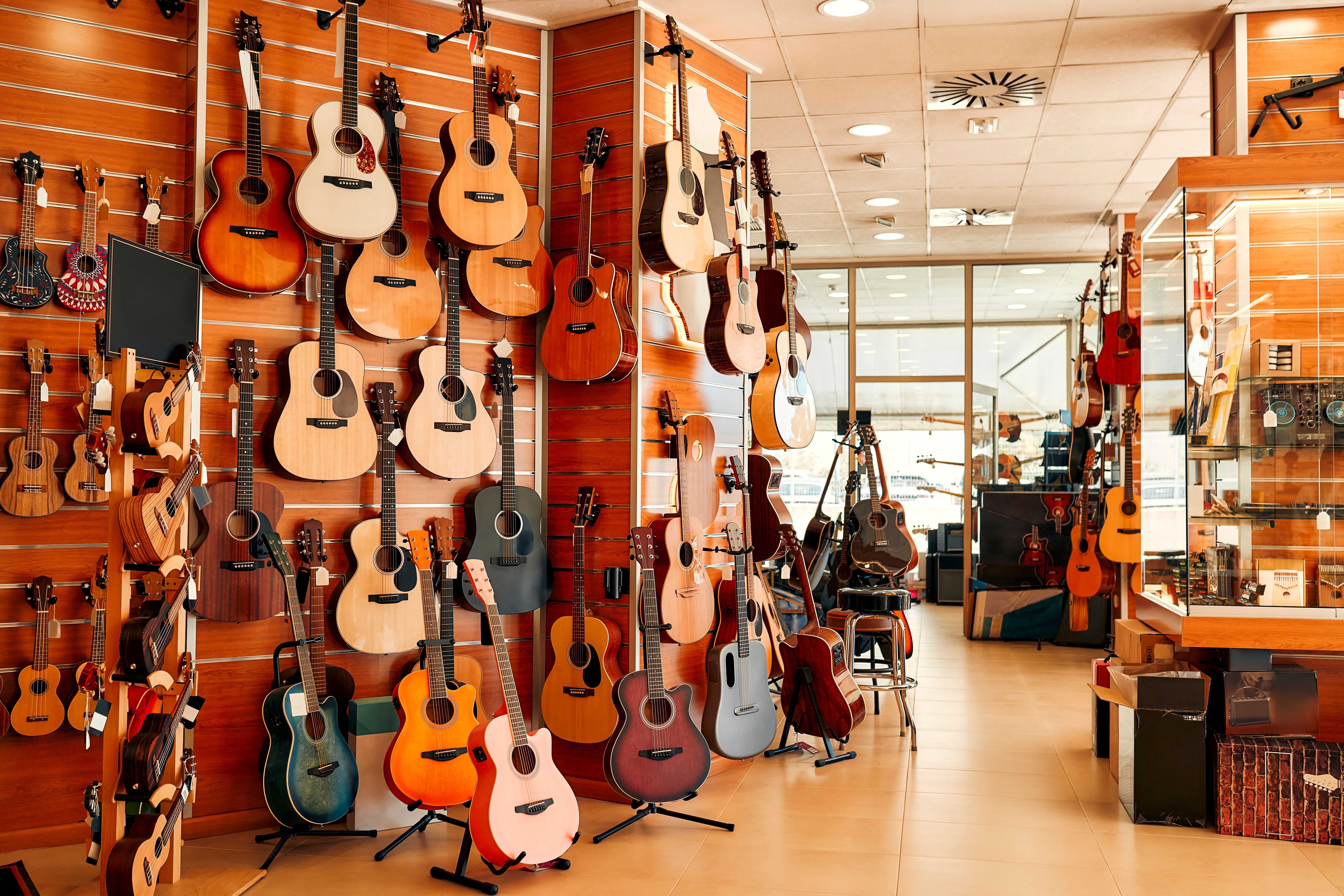 A music store displays a large variety of acoustic guitars on wooden walls, showcasing different shapes and styles