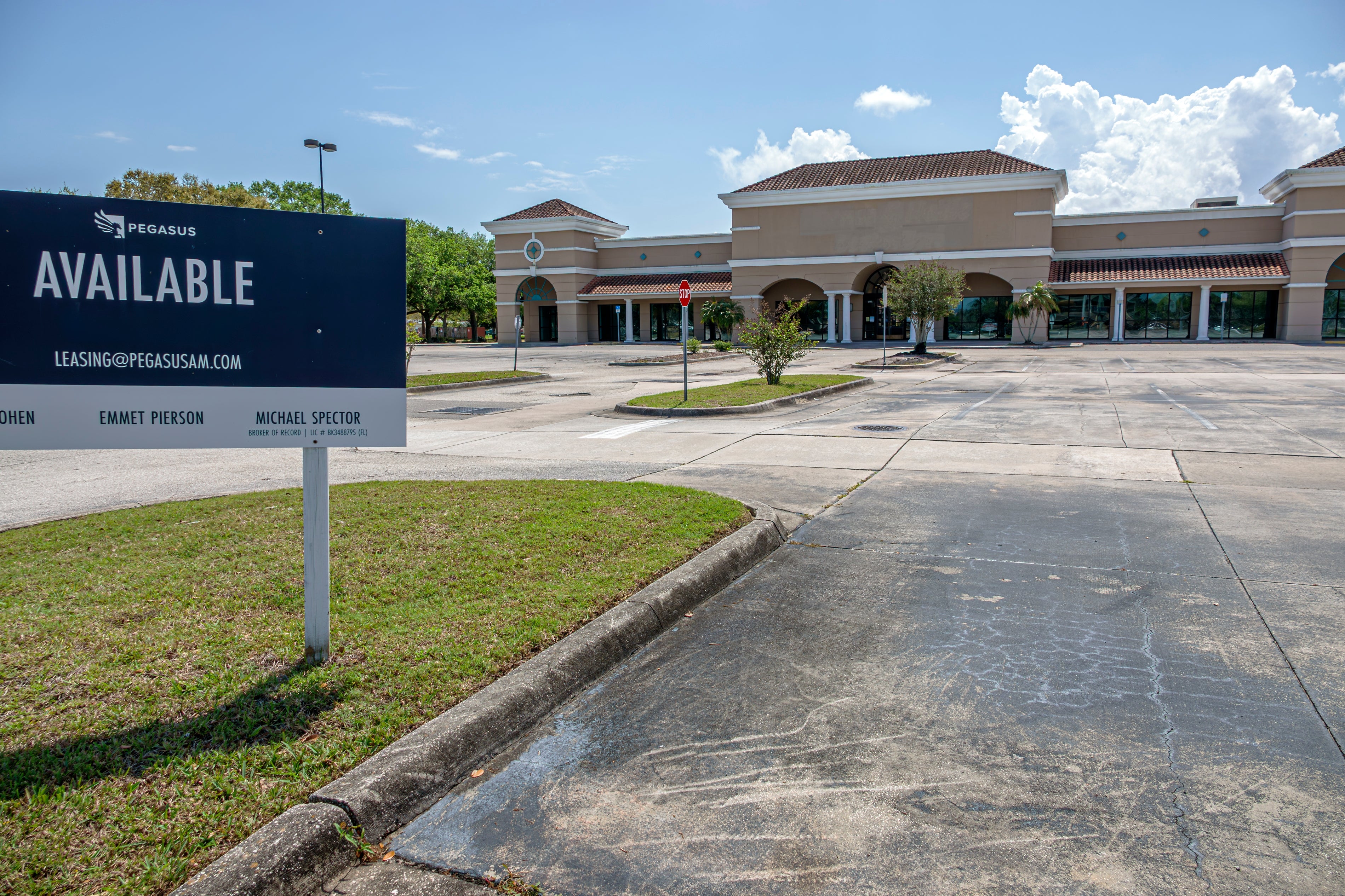 An empty parking lot in front of a strip mall with a sign showing leasing information