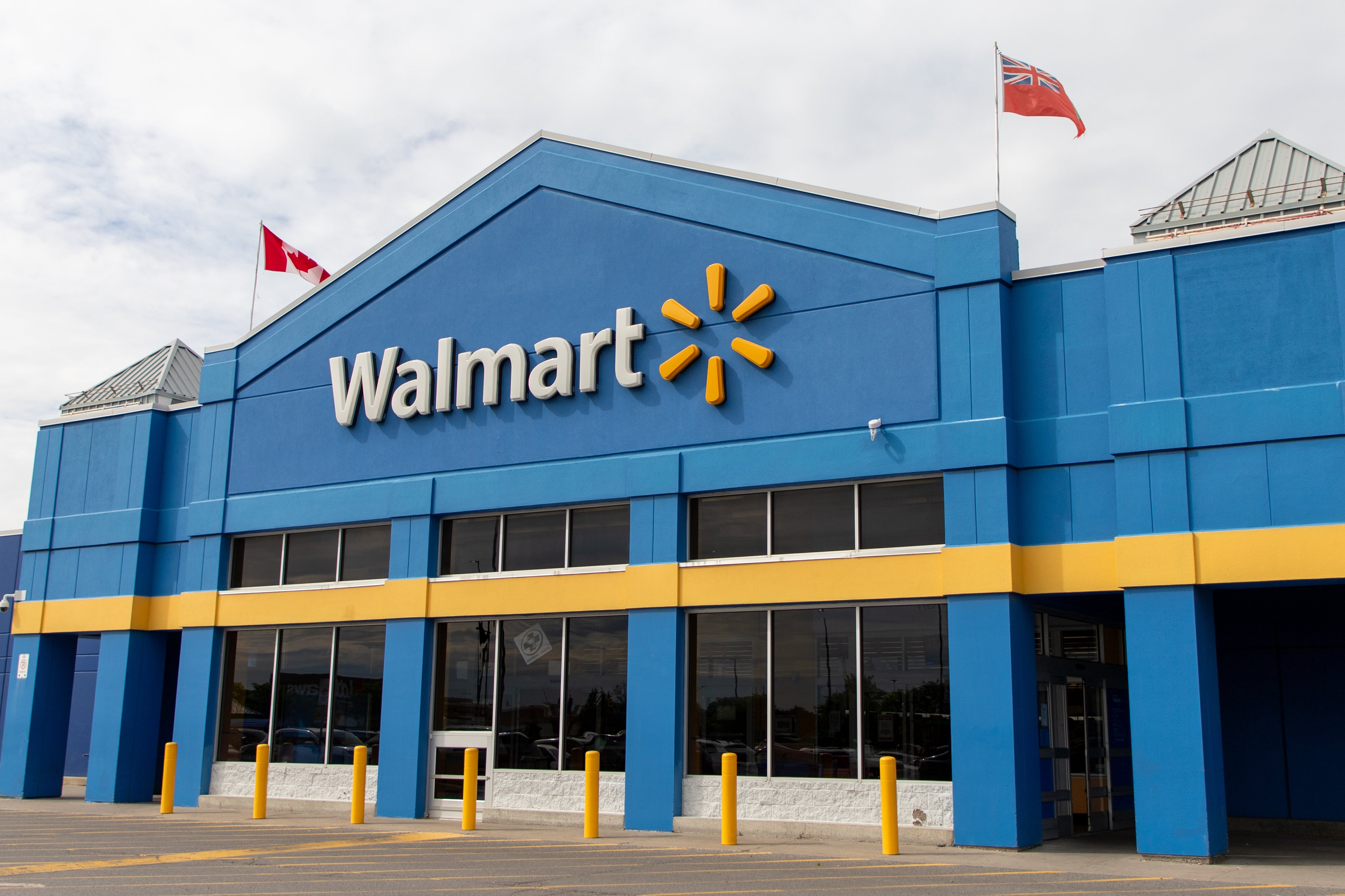 Walmart storefront with Canadian and provincial flags flying above, showcasing its distinctive logo and entrance