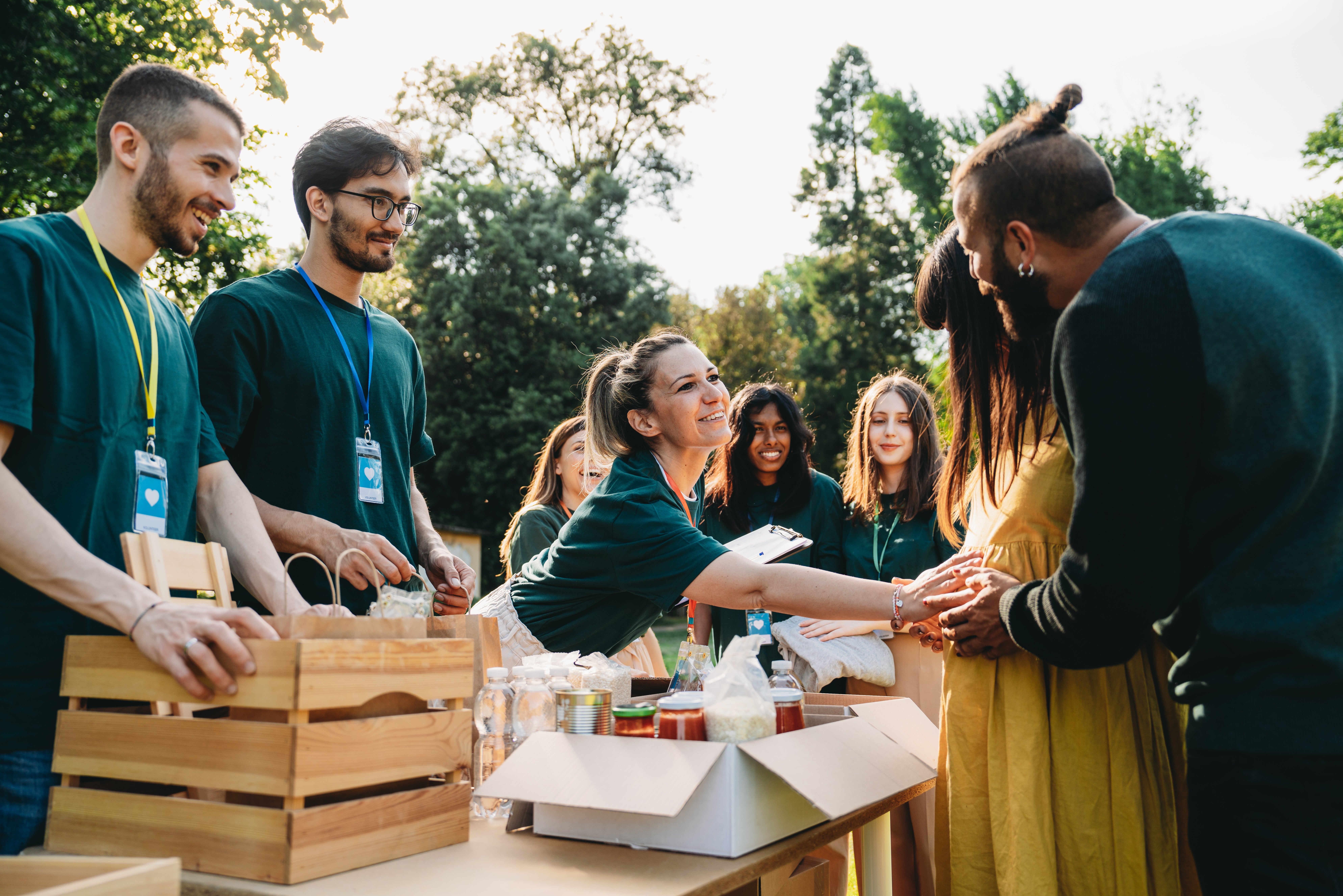 Volunteers with name tags distribute food items outdoors, smiling and interacting with people in line