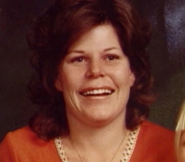 Smiling idiosyncratic   with medium-length curly hair, wearing a necklace and open-collared top