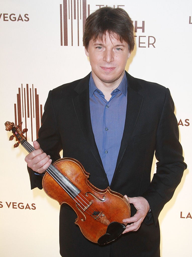 Person holding a violin, wearing a suit   with a bluish  shirt, astatine  an lawsuit   backdrop with text