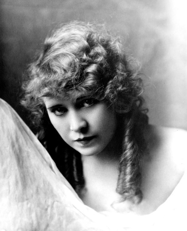 Vintage representation    of a idiosyncratic   with long, wavy hair, gazing straight  astatine  the camera with a brushed  expression, holding a draped fabric