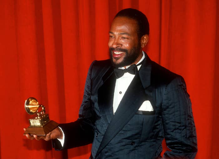 Orang bertuksedo memegang penghargaan Grammy, berdiri di depan tirai