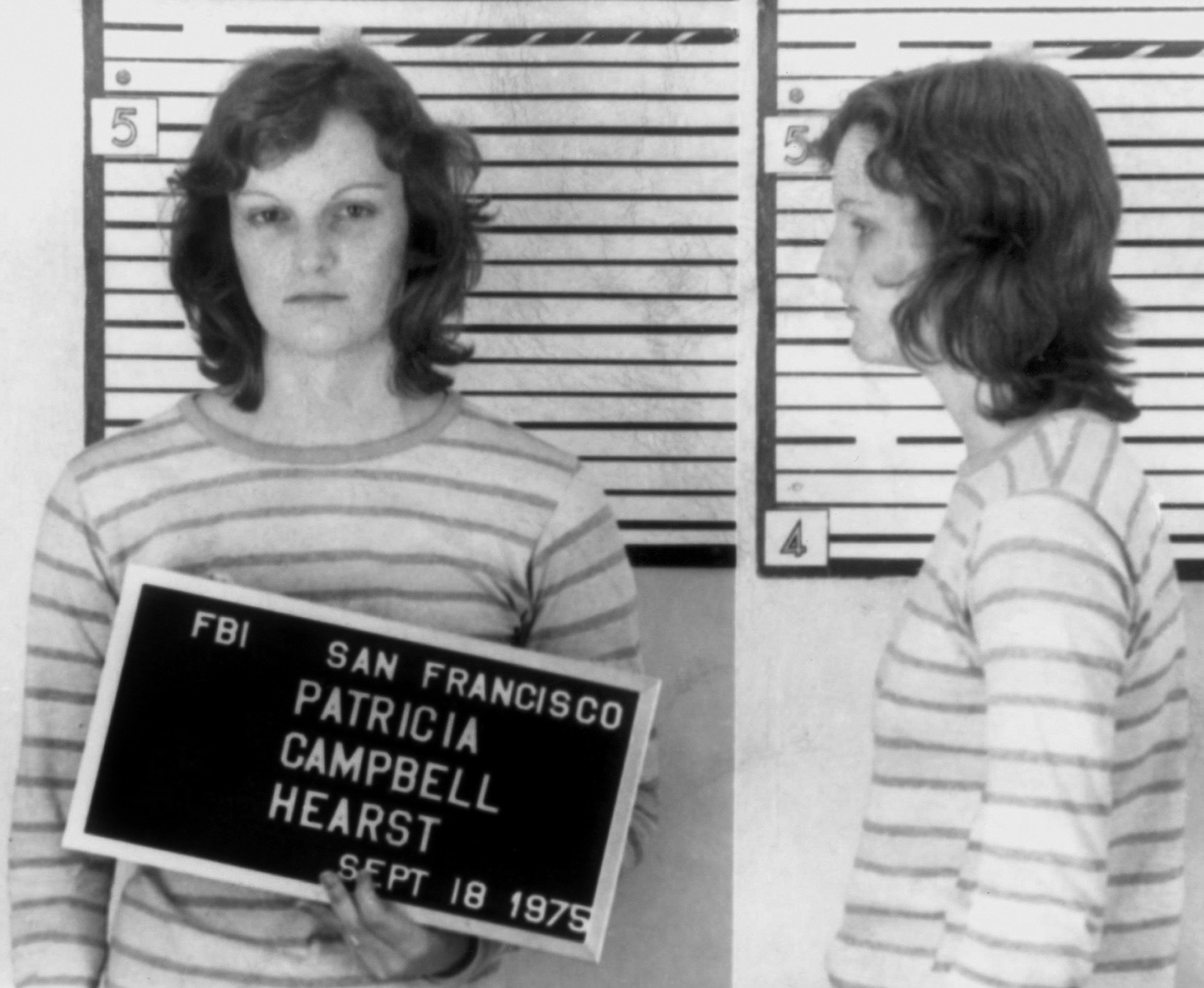 Foto Patricia Hearst tahun 1975, mengenakan kemeja bergaris, memegang papan identifikasi dengan rincian FBI, ditampilkan di depan dan tampilan profil