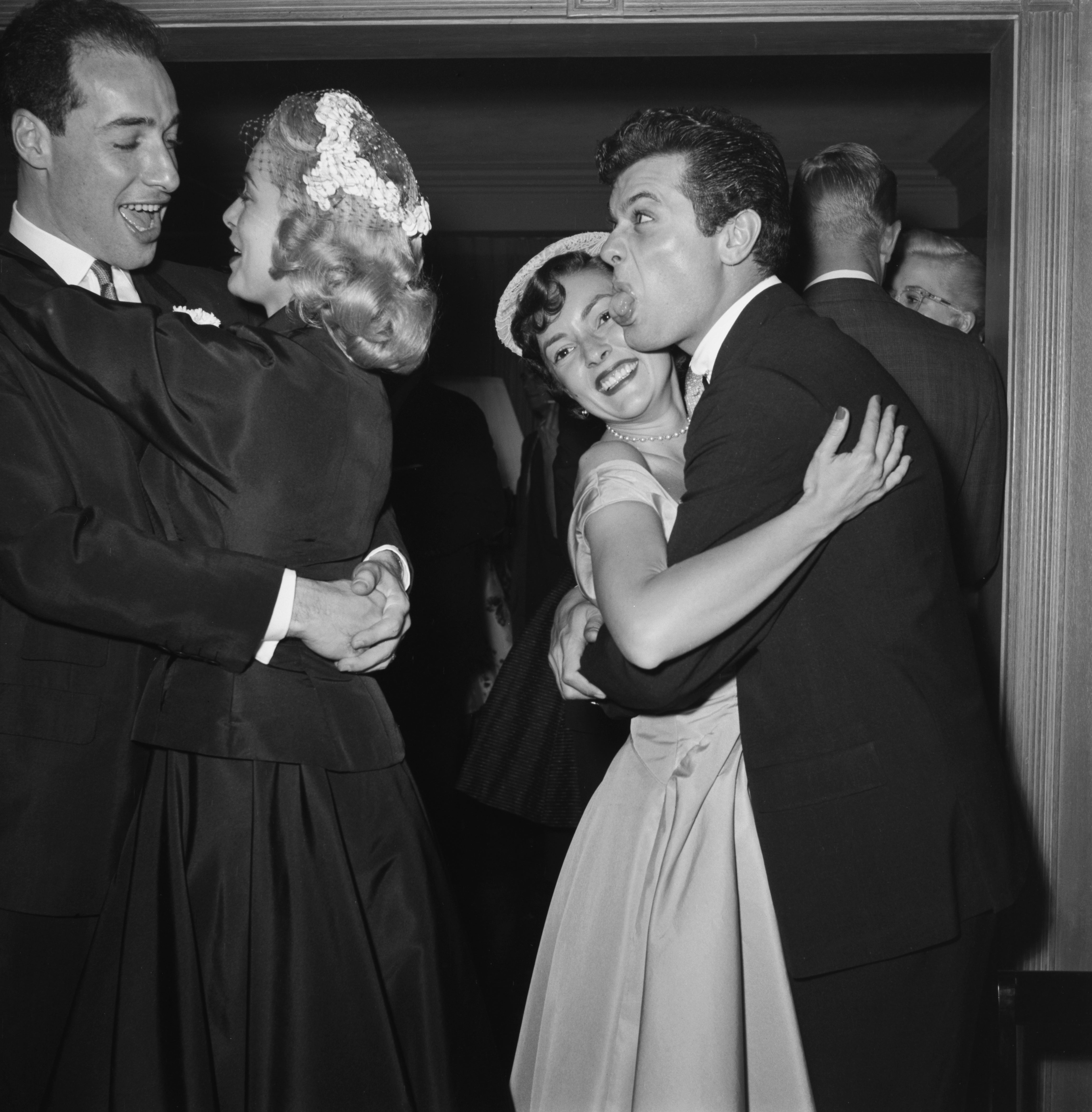 Tony Curtis sticking his tongue out at Janet Leigh as they both hug other people in party attire