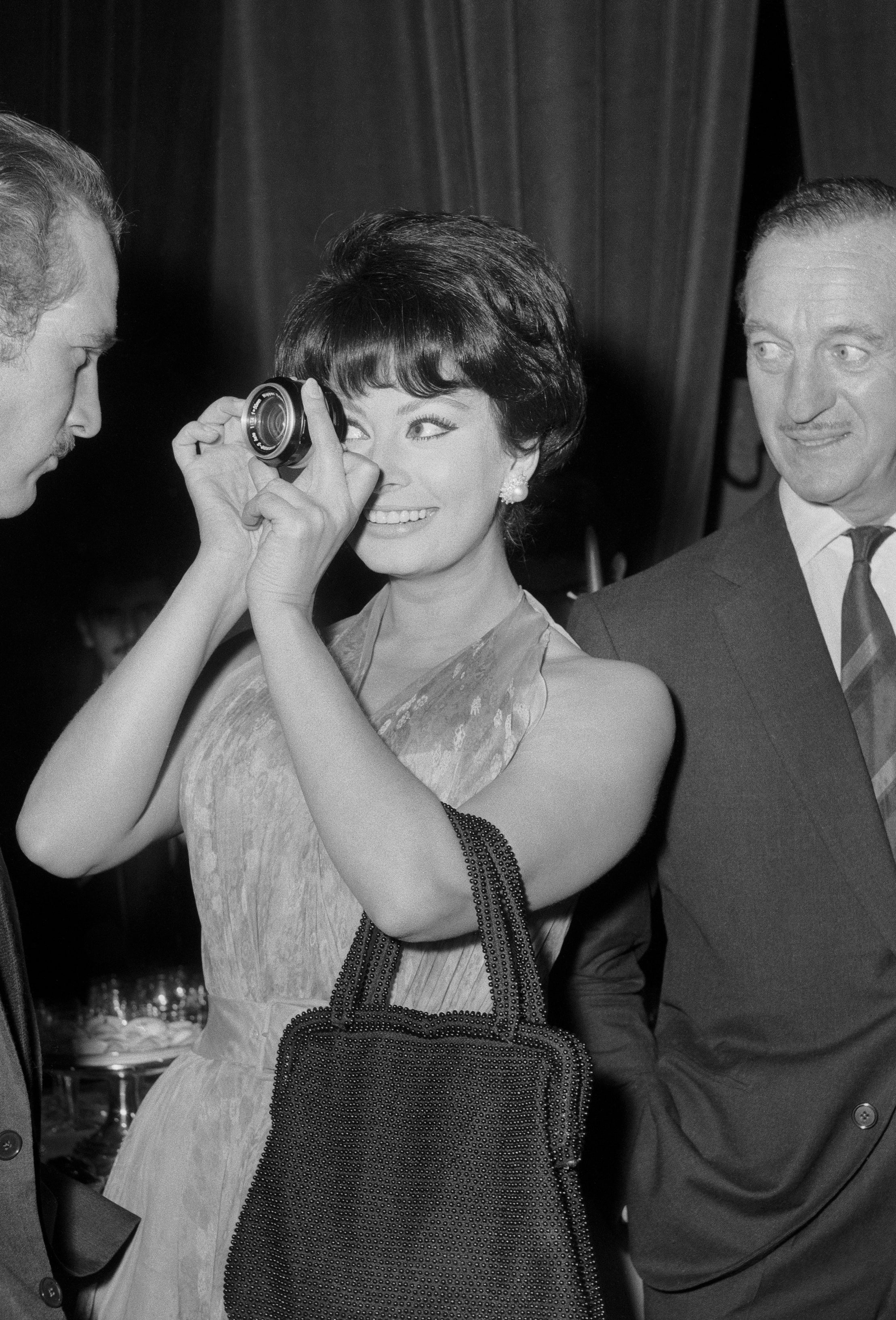Sofia Loren playfully looks through a lens at a Paul Newman in a suit at an event