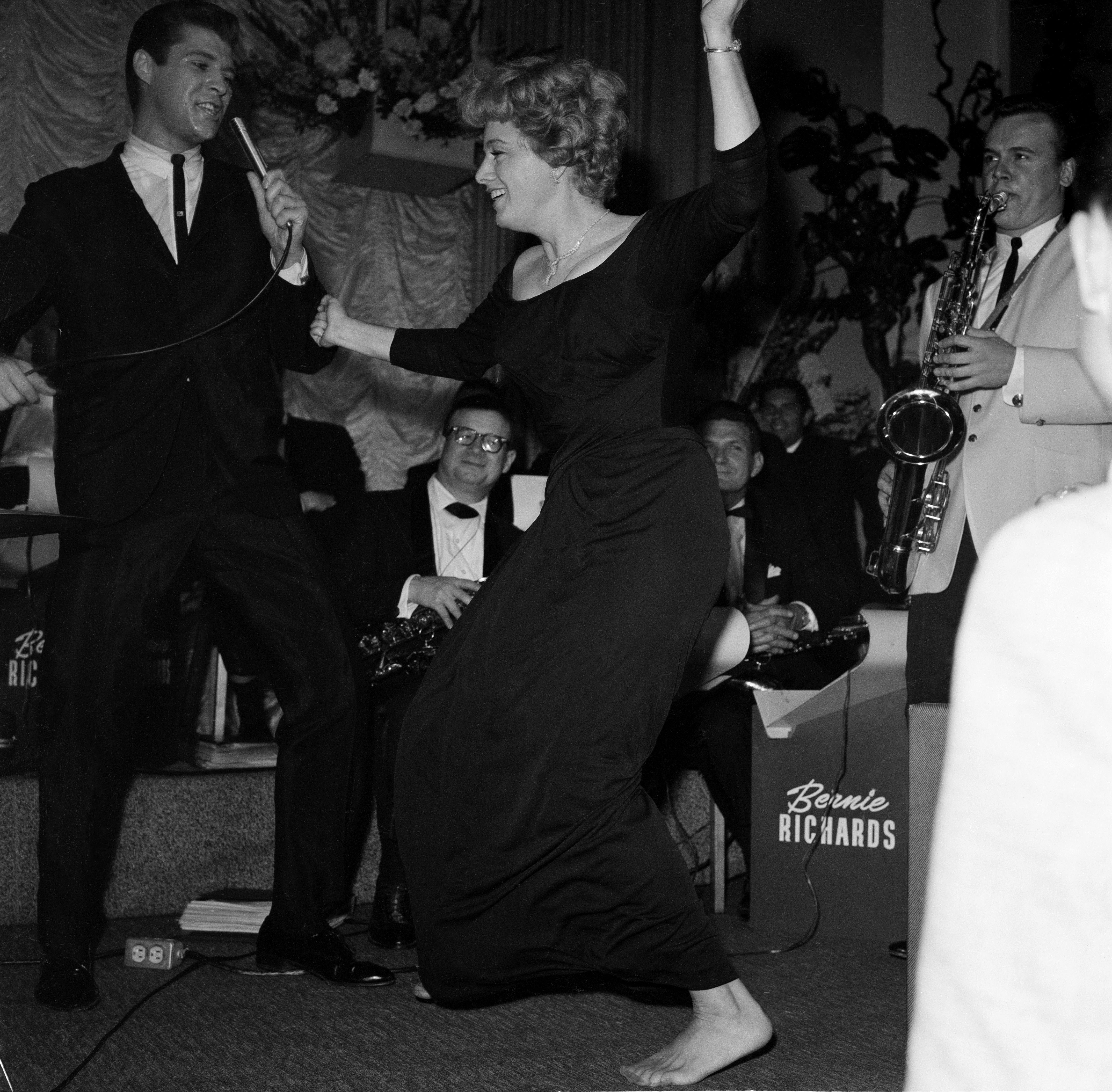 Shelley Winters dancing energetically at a lively event, with band members playing instruments in the background