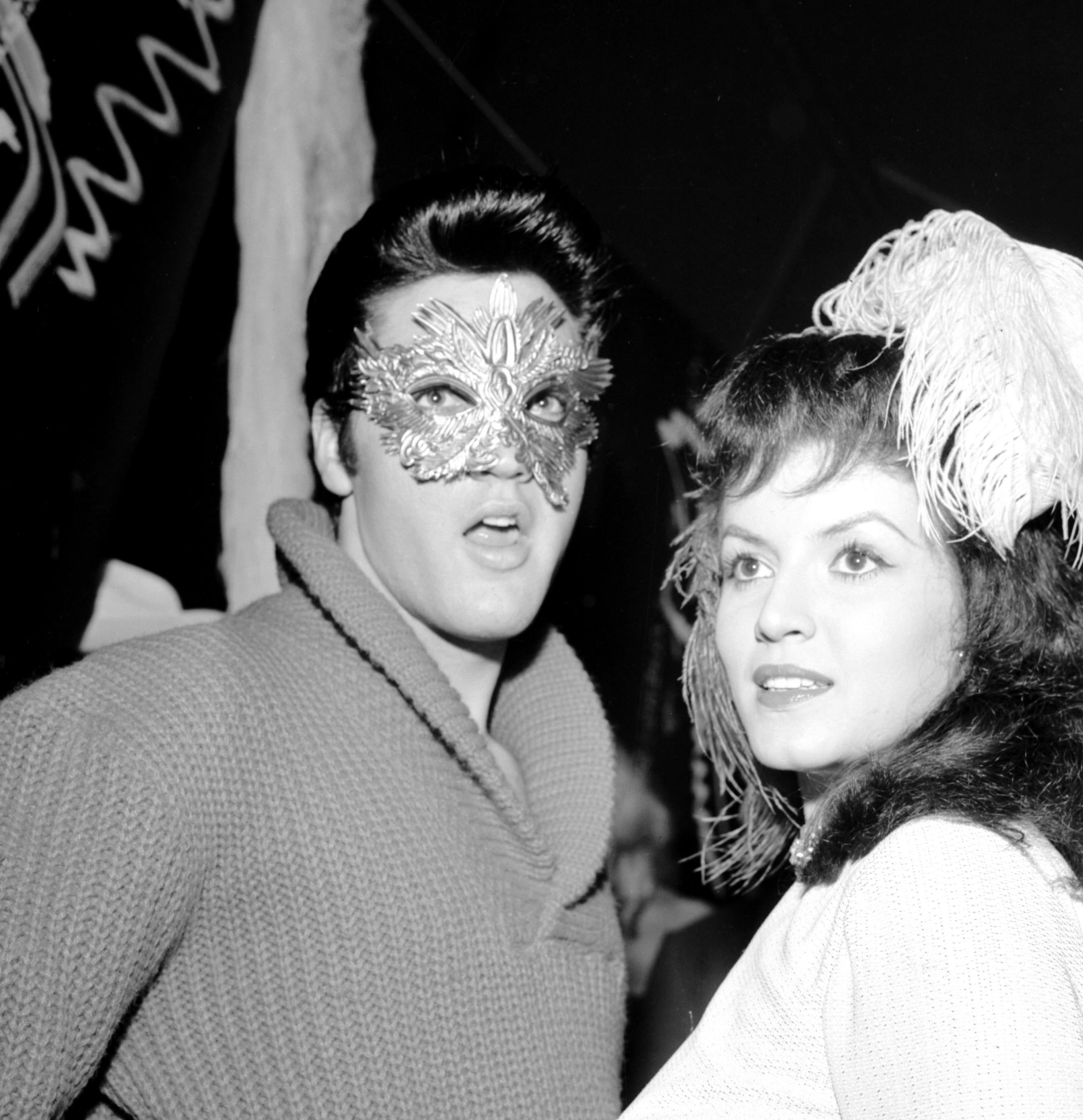 Elvis Presley and Joan Bradshaw  at a masked event, when Elvis in a masquerade mask and Joan with a feather in her hair