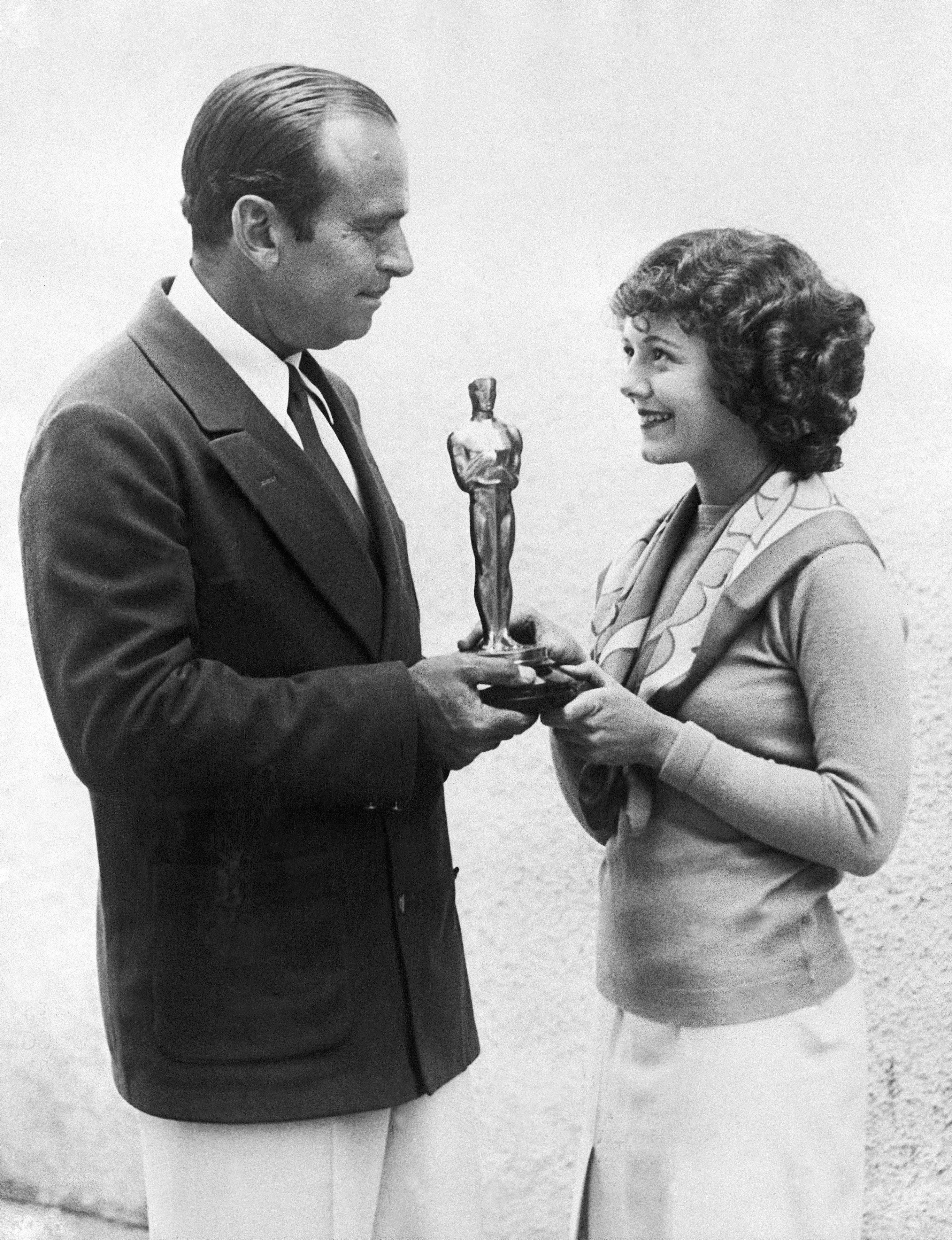 Douglas Fairbanks presenting Janet Gaynor with an Oscar statuette between them, with her smiling broadly