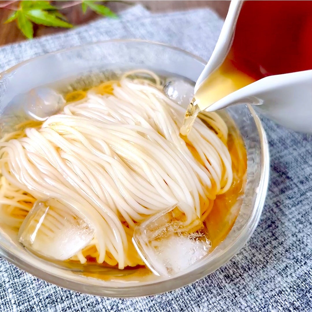 そうめんにつゆを注いでいる様子。ガラスの器に麺と氷が入っている。