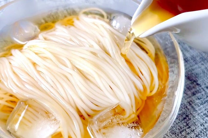 そうめんにつゆを注いでいる様子。ガラスの器に麺と氷が入っている。