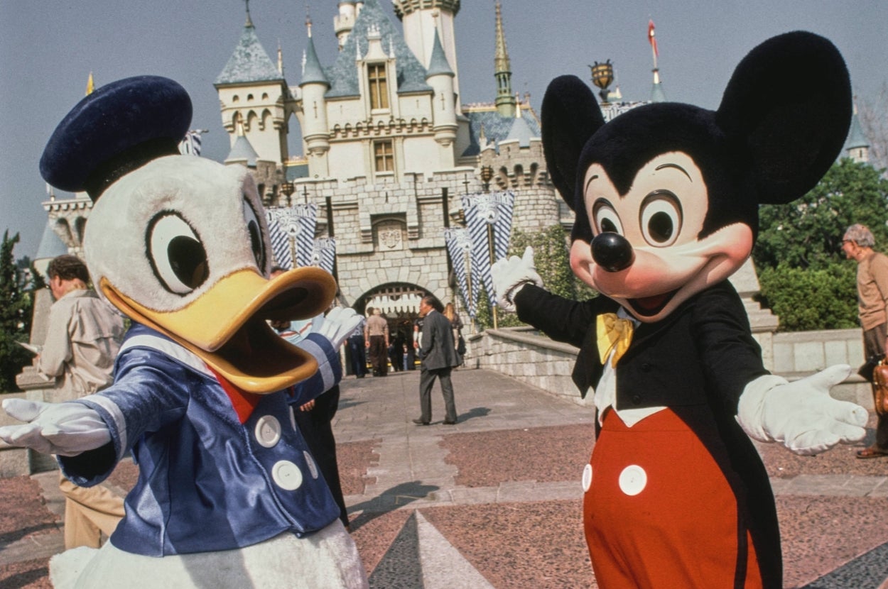 Mickey Mouse and Donald Duck characters pose happily in front of a famous castle at a theme park, welcoming visitors