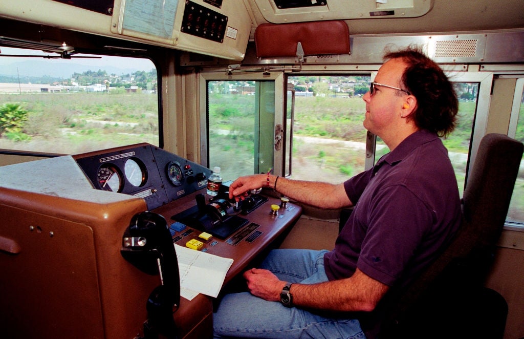 Person operating a train's control panel, focused on the tracks ahead, with countryside visible through windows