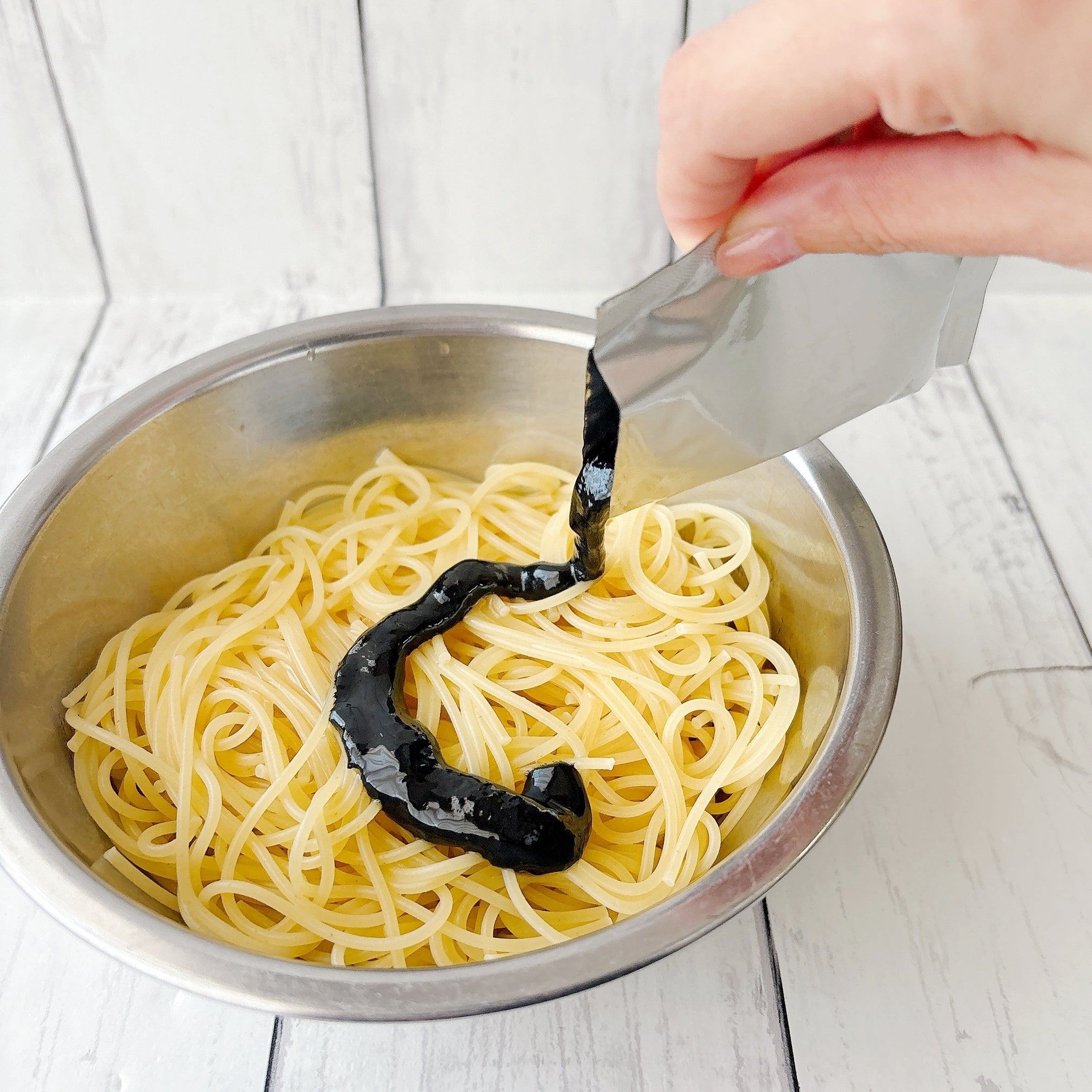無印良品の「あえるだけのパスタソース いかすみ」手がパスタにいかすみソースをかけている。