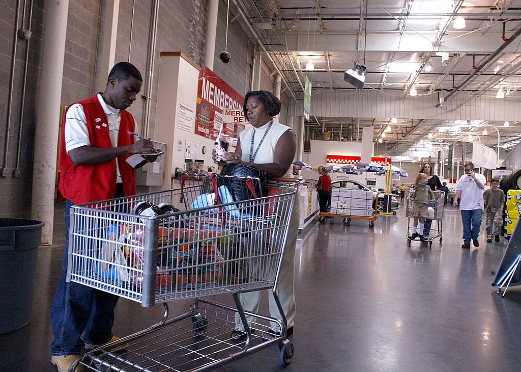 Store employee checks receipt for customer with a full cart in a warehouse-style store aisle